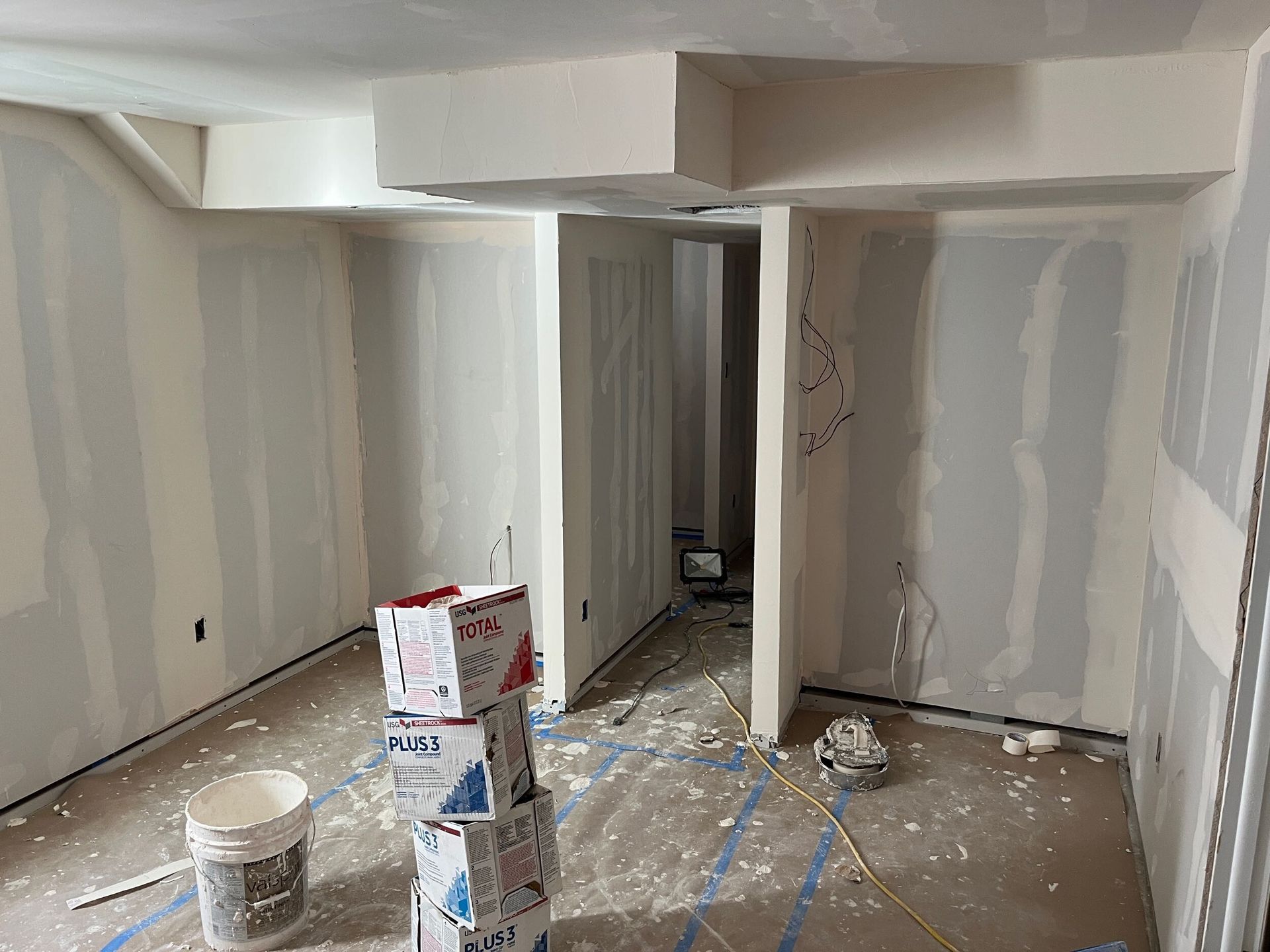 Partially renovated room with taped drywall, paint buckets, and construction debris on the floor