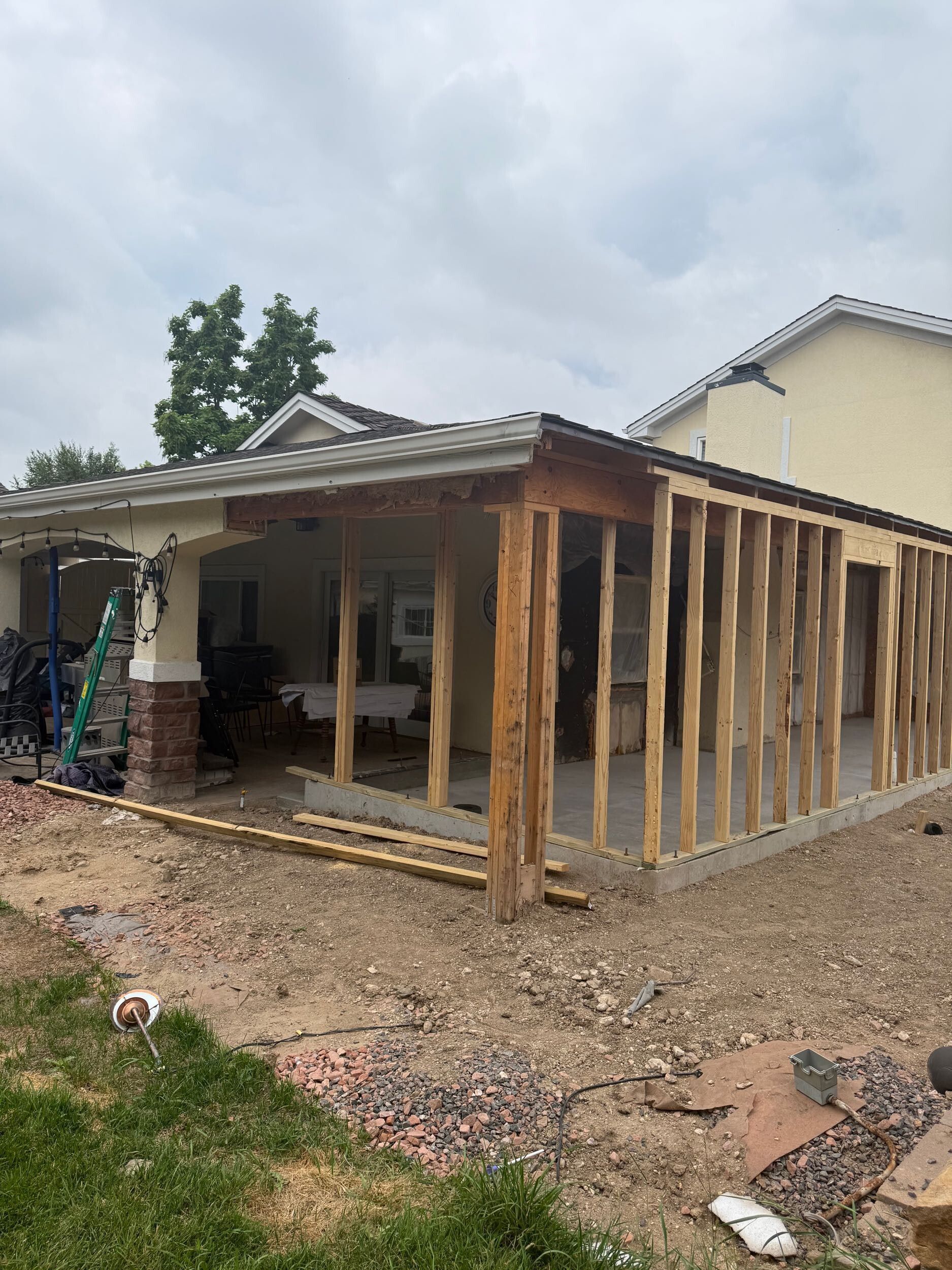 Partially built wooden house frame with open porch in a muddy yard under cloudy skies