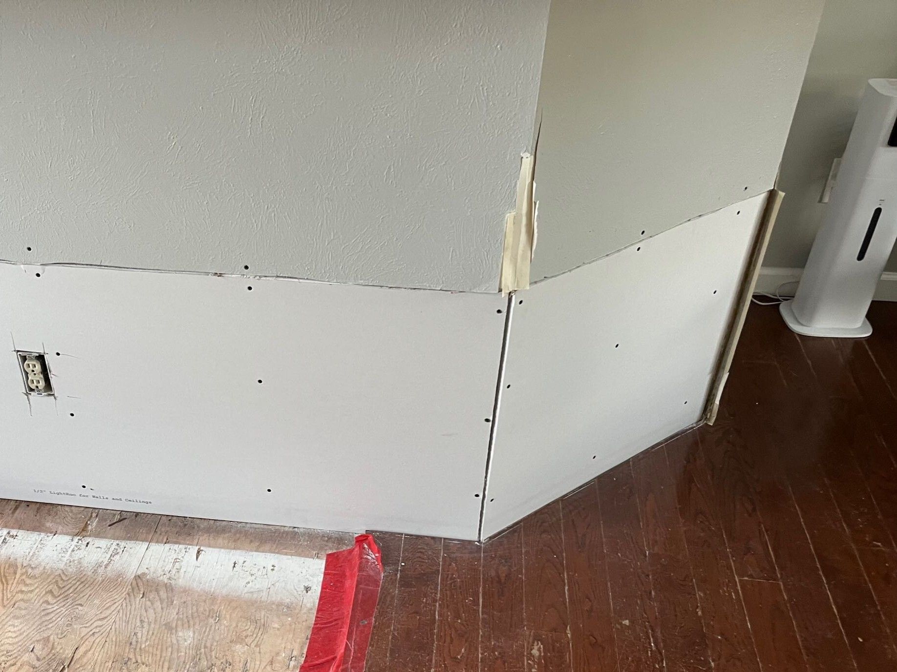 Damaged interior wall corner with exposed drywall and scuffed baseboard over wood floor