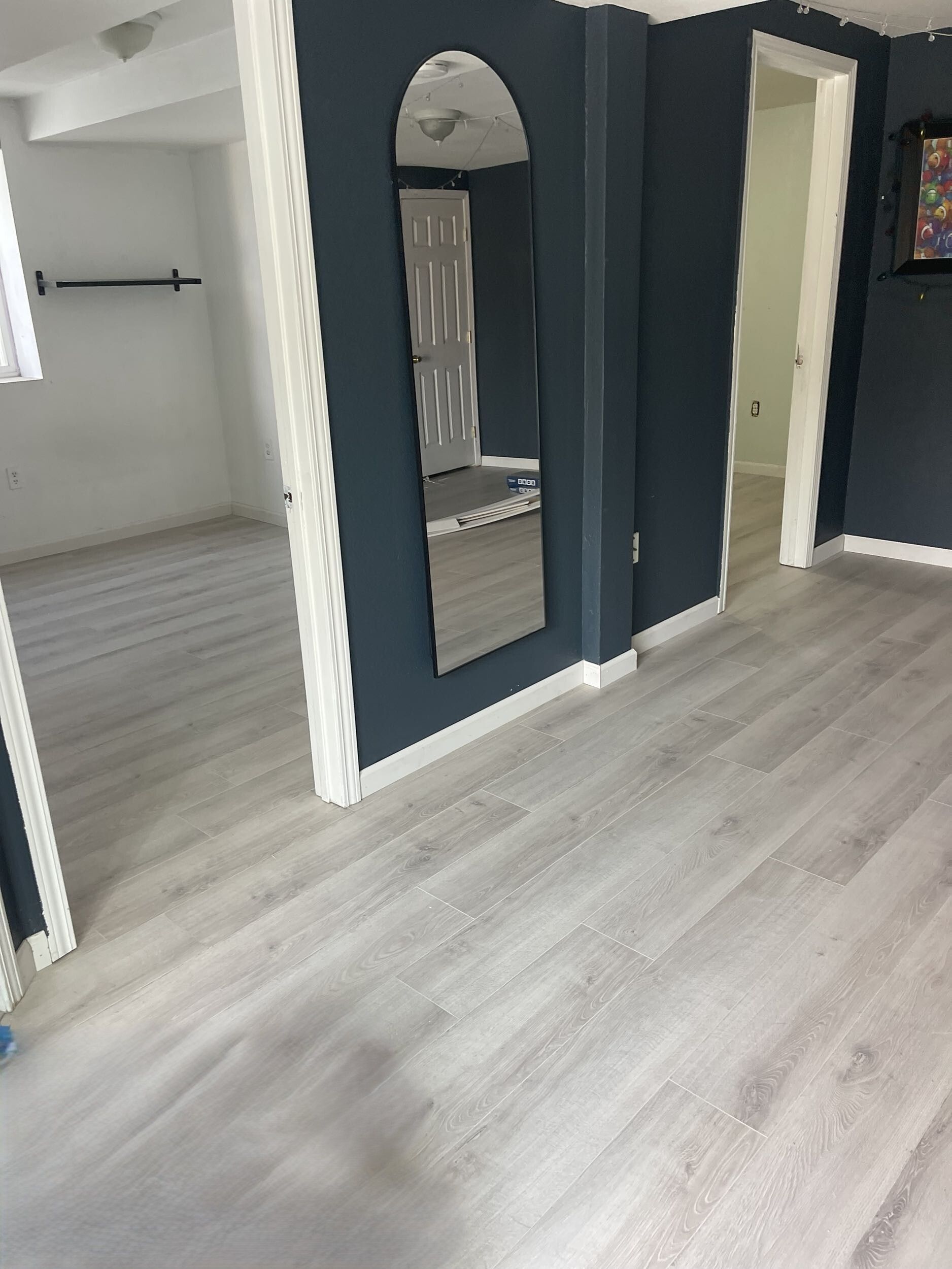 Empty hallway with gray wood flooring, dark blue accent walls, and mirrored closet doors.