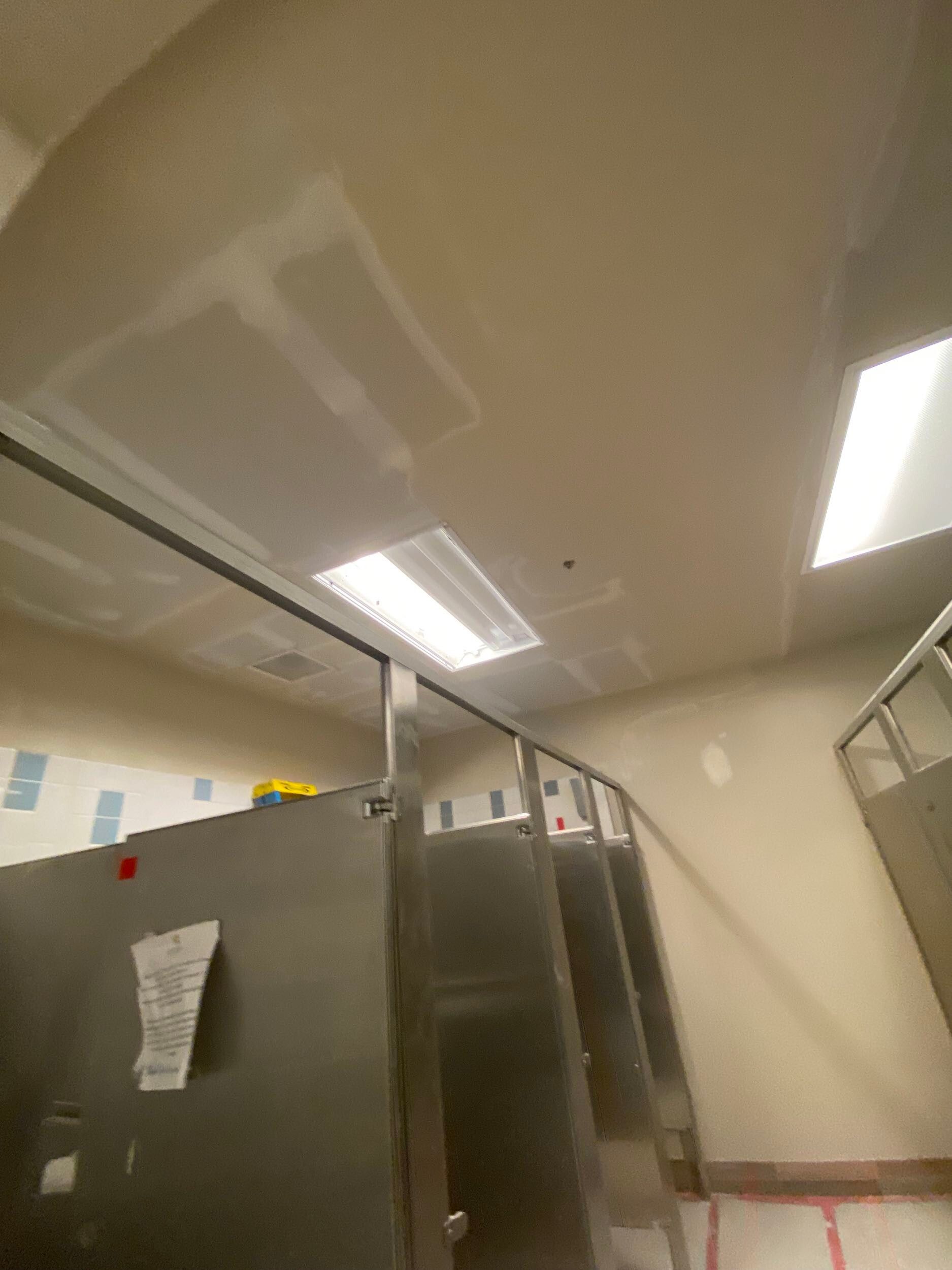 Bathroom stall ceiling with fluorescent lights and a door ajar, showing a restroom interior
