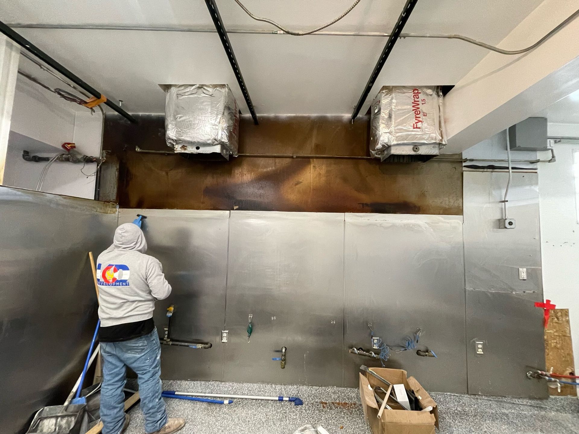 Worker painting a metallic wall in a room under renovation, with tools and ductwork overhead