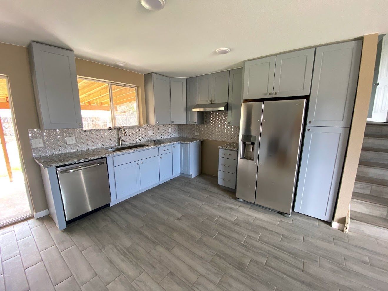 Bright kitchen with gray cabinets, stainless steel appliances, and light wood flooring