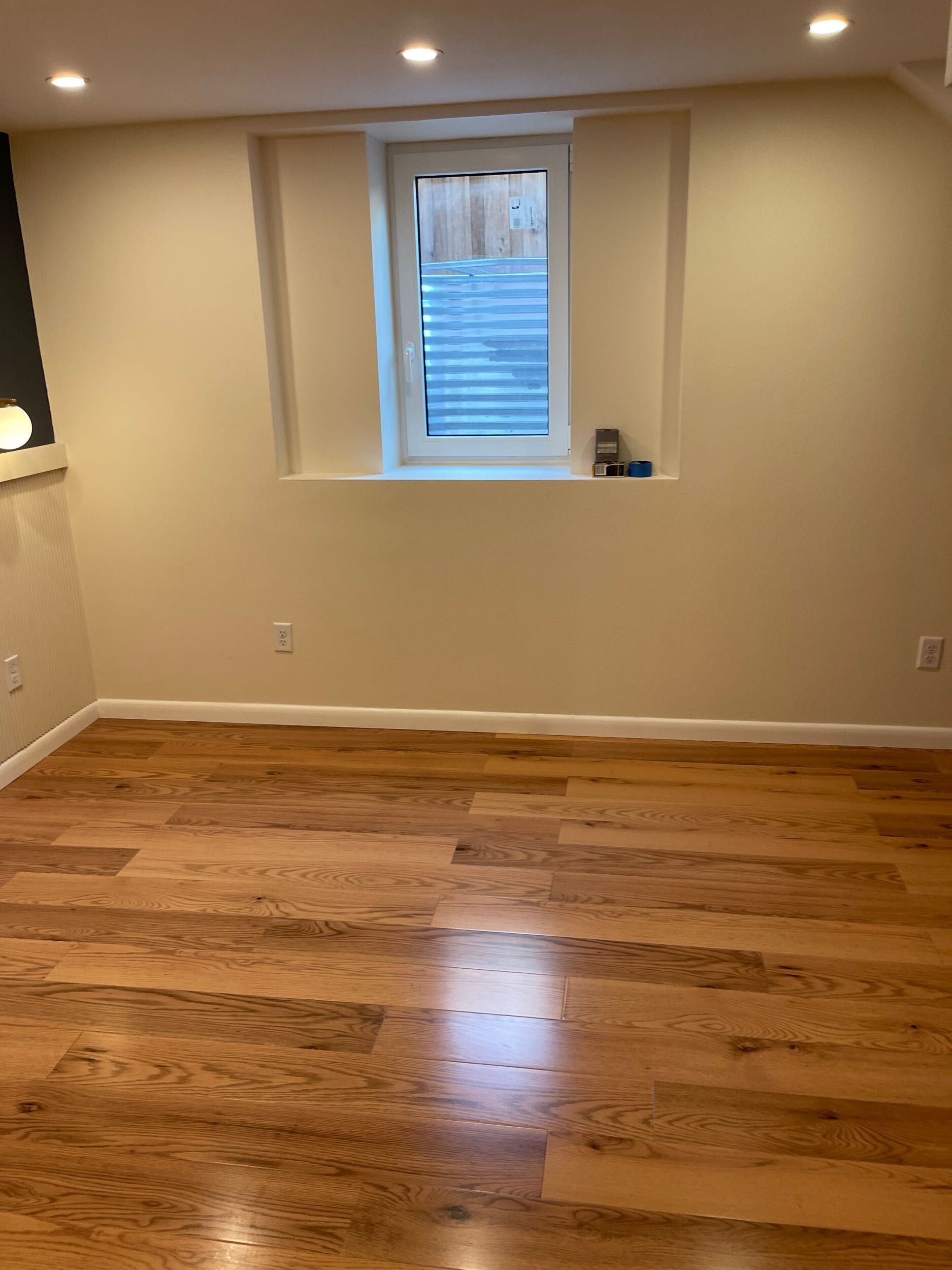 Empty room with hardwood floors, beige walls, recessed lights, and a small window.