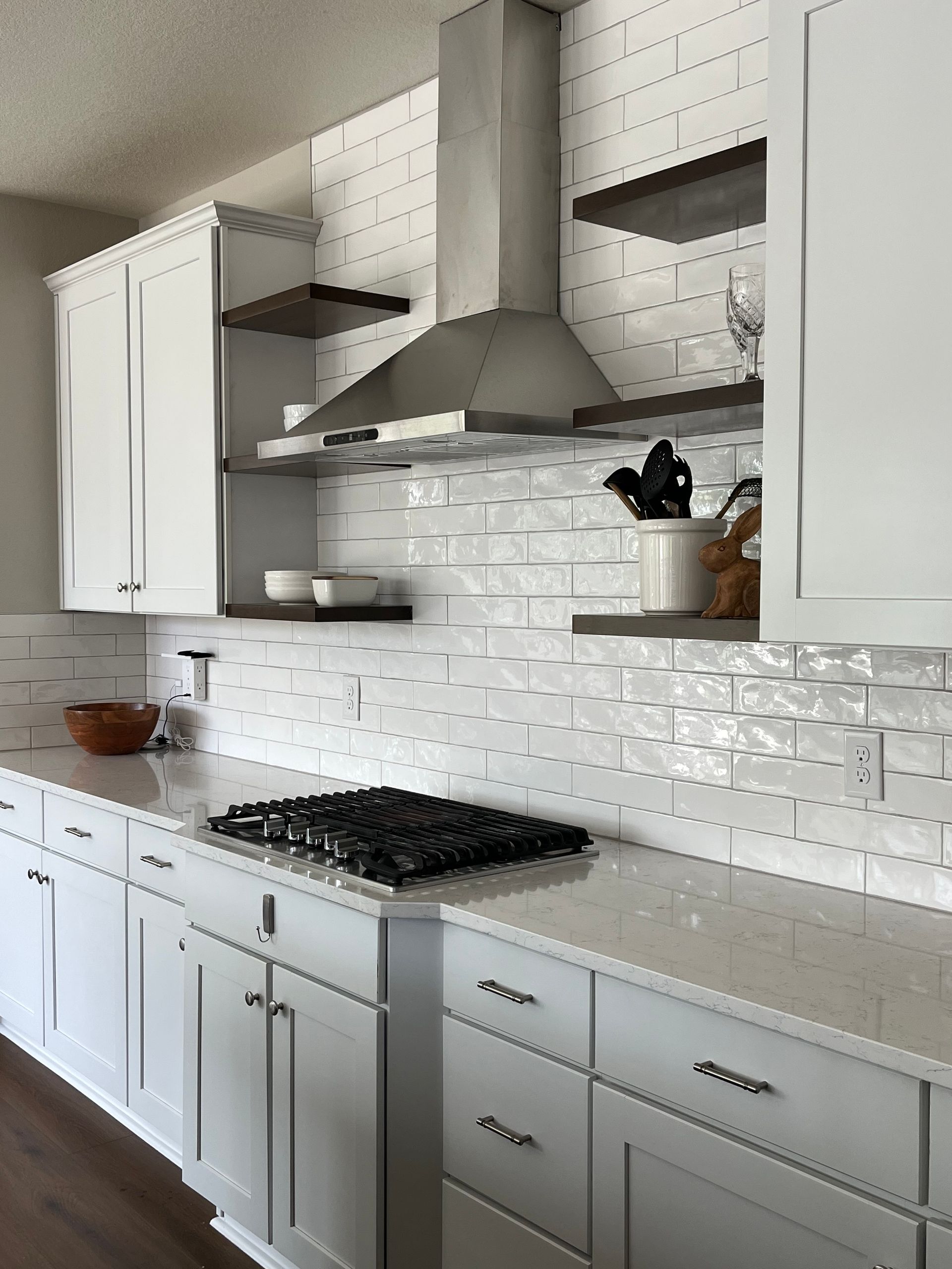 Modern white kitchen with stainless steel range hood, gray cabinets, and white brick backsplash.