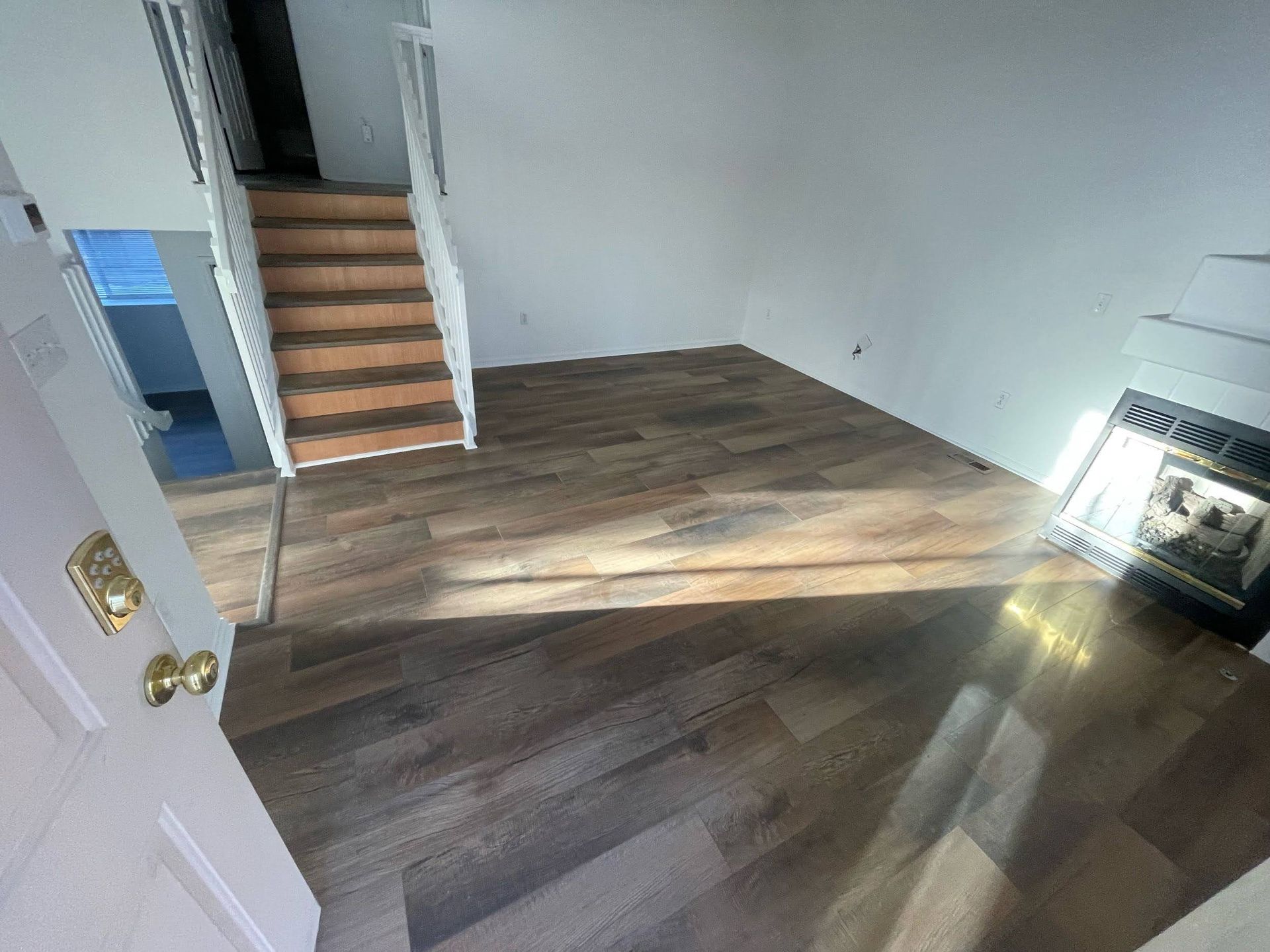 Empty room with wood flooring, stairs, and sunlight streaming through a window.