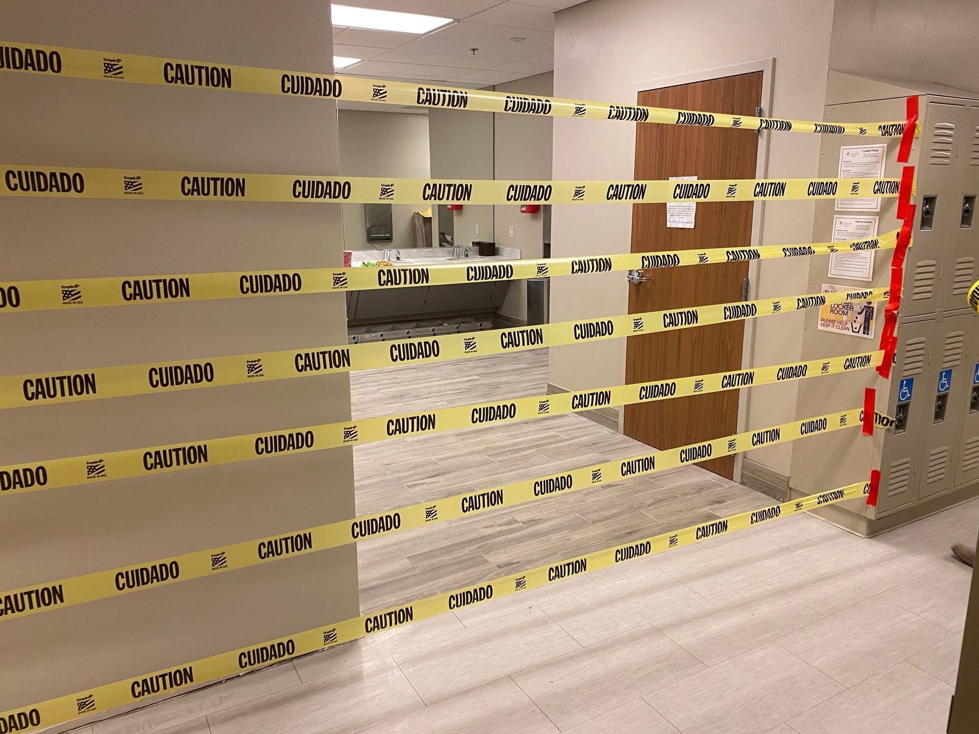 Yellow caution tape blocking a hallway outside a room with a reception desk and red lockers