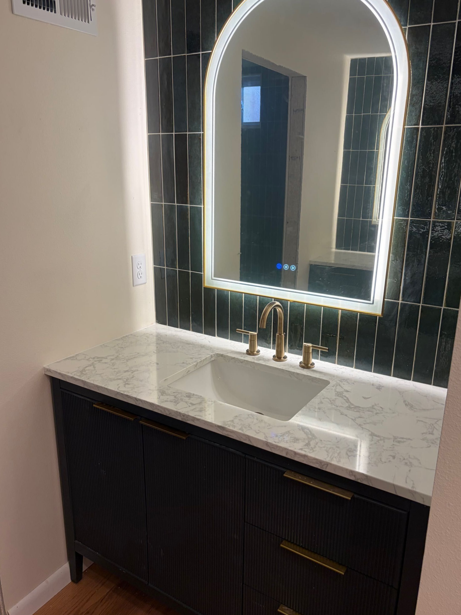 Bathroom vanity with marble countertop, round mirror, black cabinets, and gold faucet
