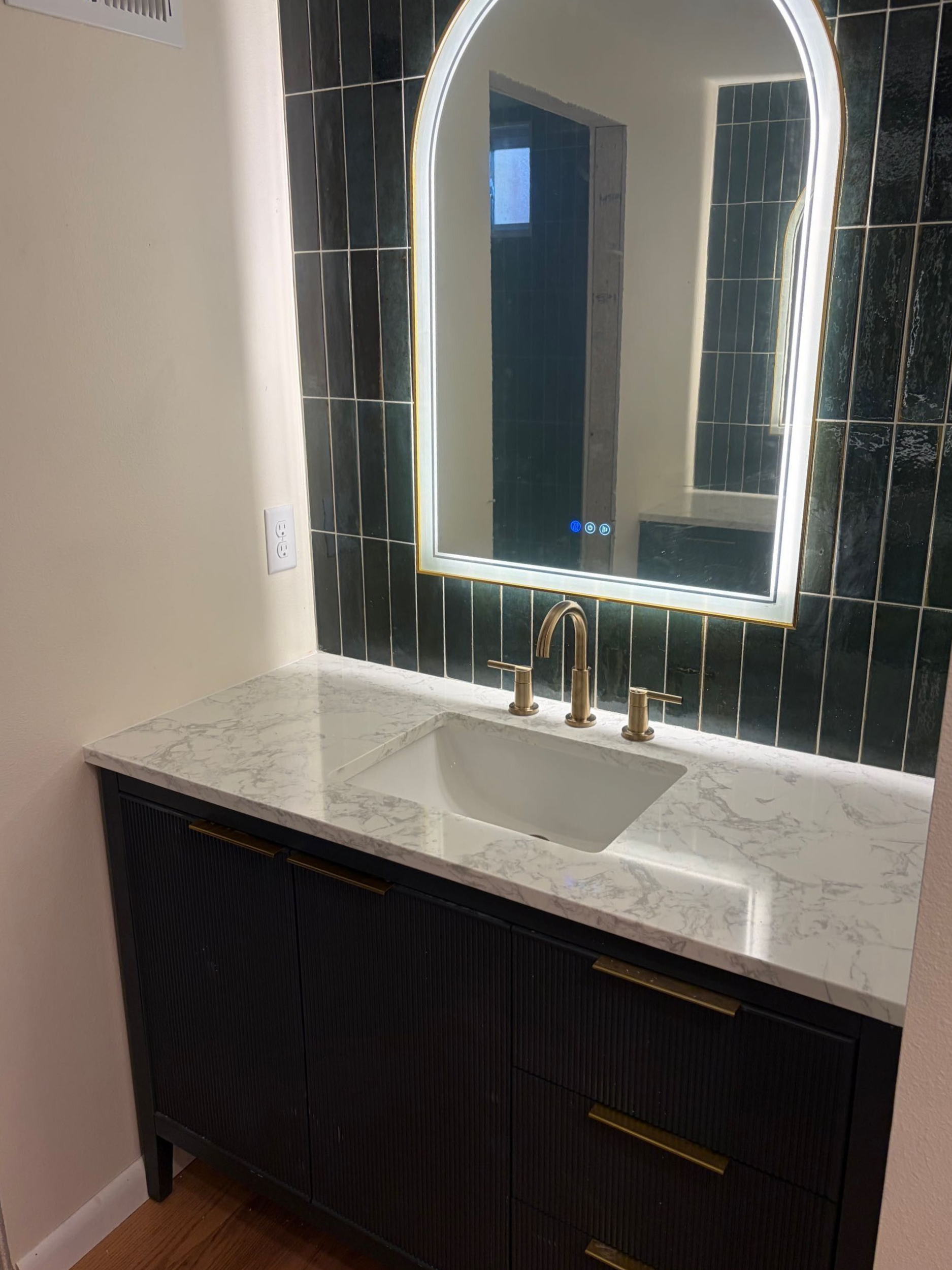 Modern bathroom vanity with illuminated arched mirror, white countertop, and dark cabinets.