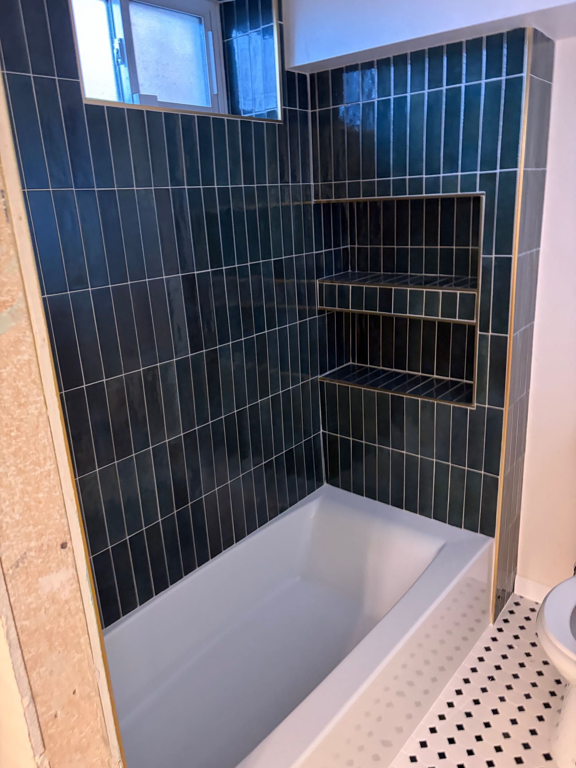 Modern tiled shower with white tub, dark blue walls, and built-in corner shelves.
