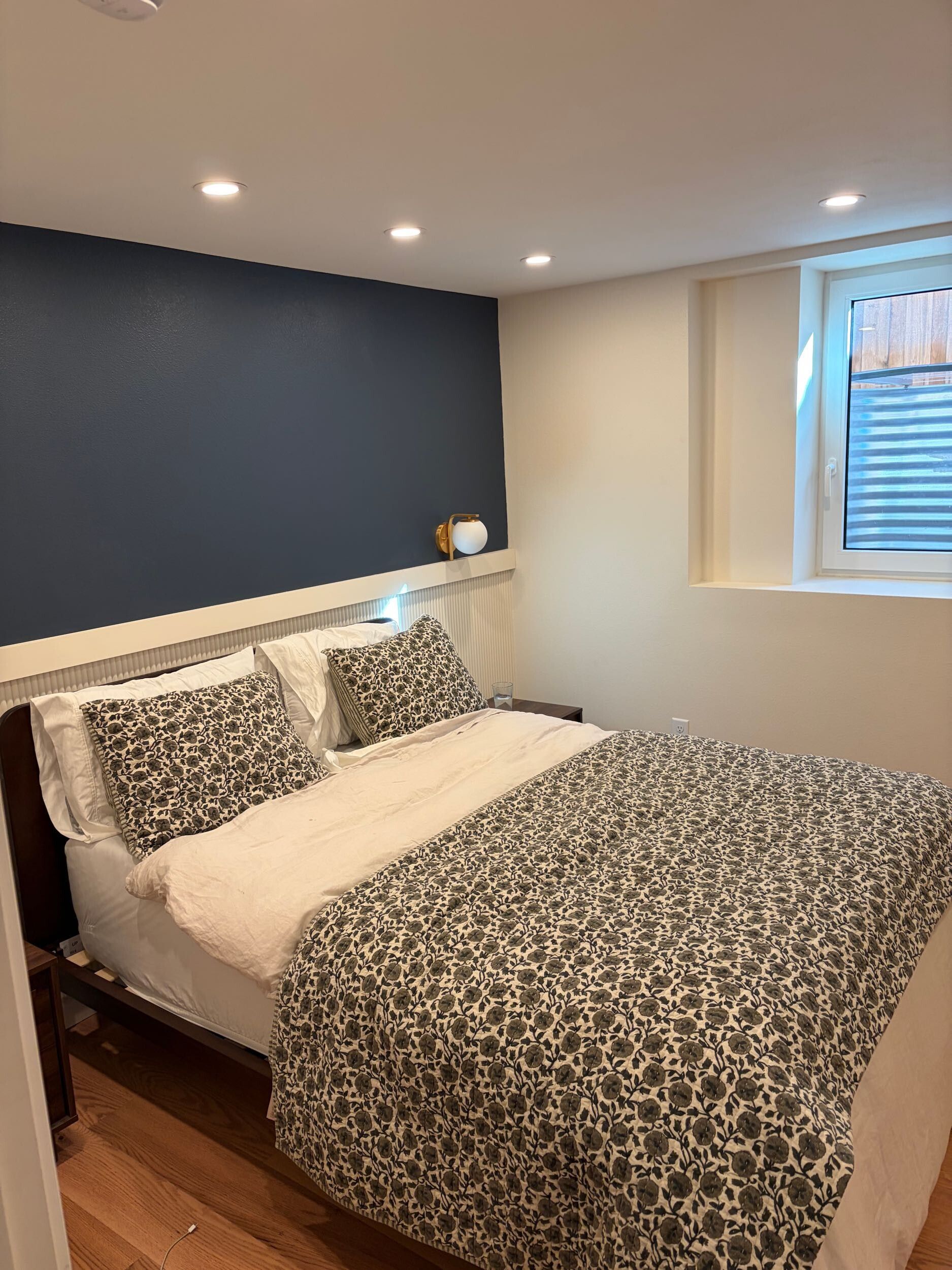 Small bedroom with a bed, patterned bedding, blue accent wall, and a window with blinds