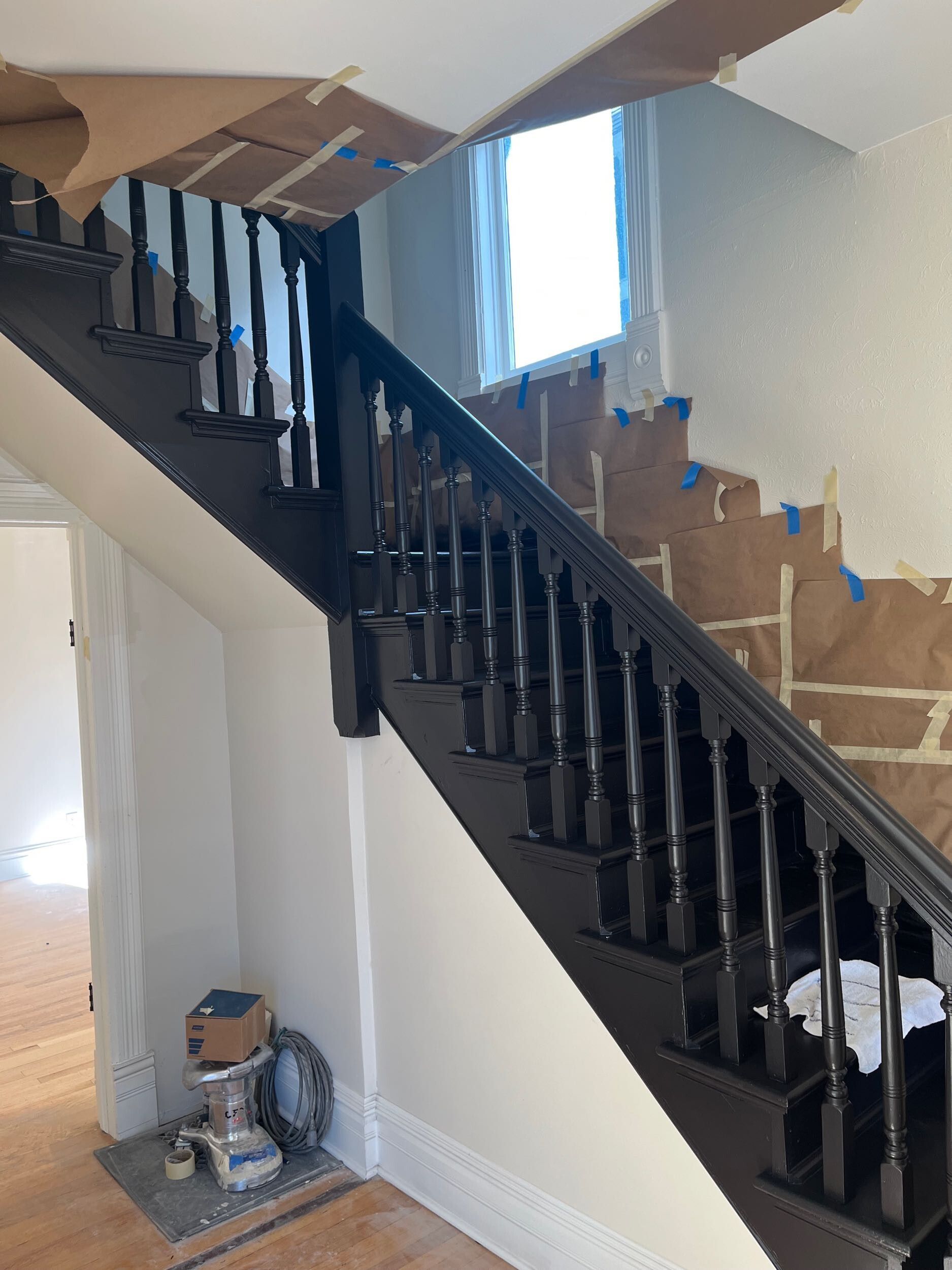 Interior staircase with black banister, cardboard boxes on the steps, and a window at the landing
