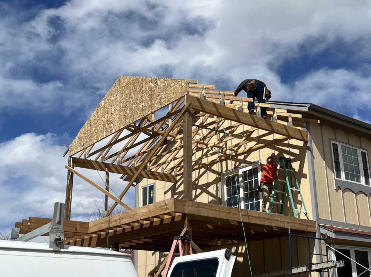 Workers building a wooden house addition under a partly cloudy sky