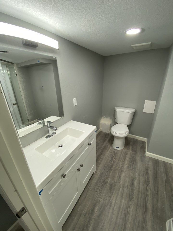 Modern bathroom with white vanity, mirror, toilet, and gray flooring.