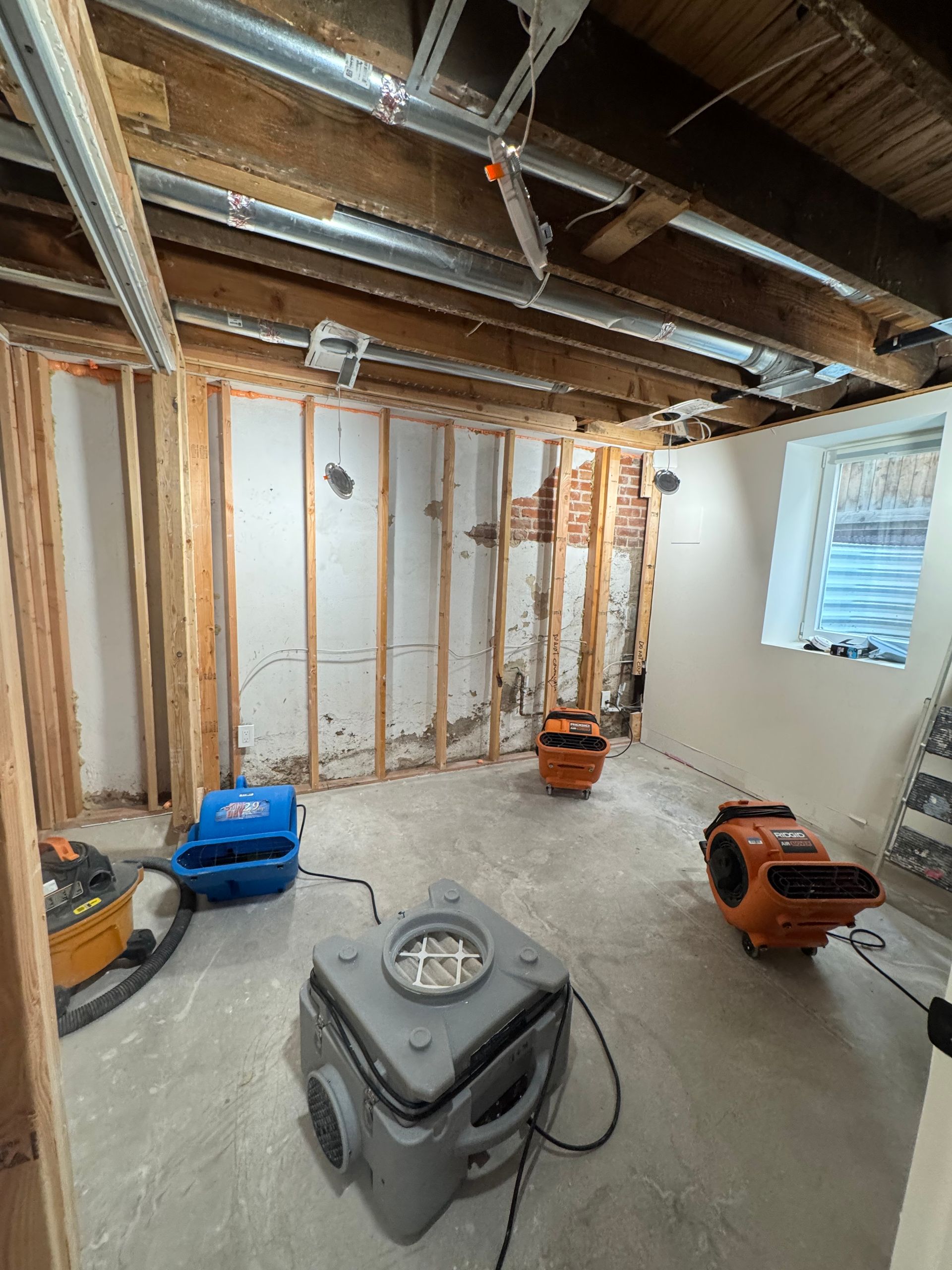 Basement under renovation with exposed studs, unfinished ceiling, and construction vacuums on concrete floor