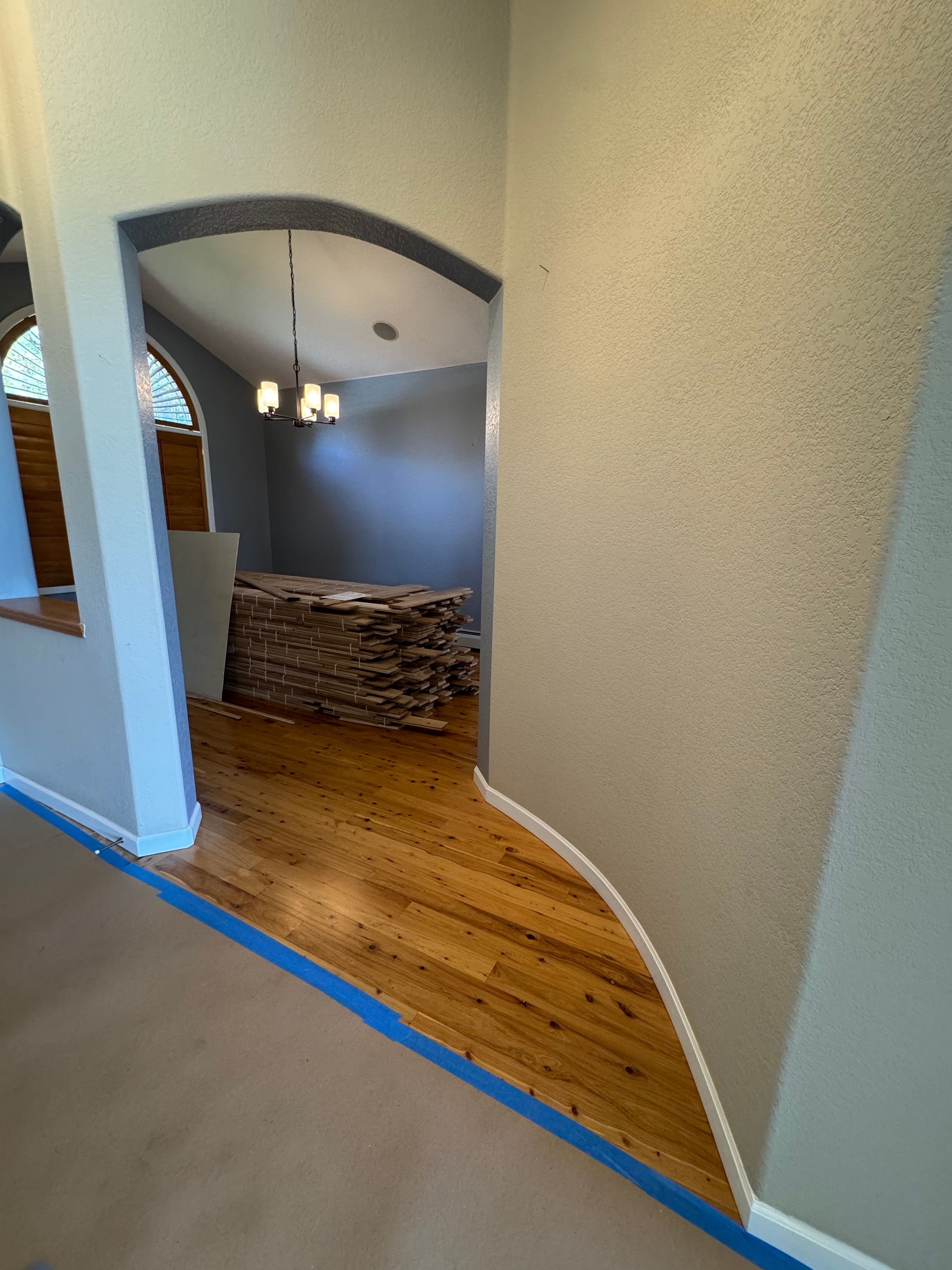 Home interior with arched doorway, blue-gray room, wood floor, and stacked firewood near a hanging light.