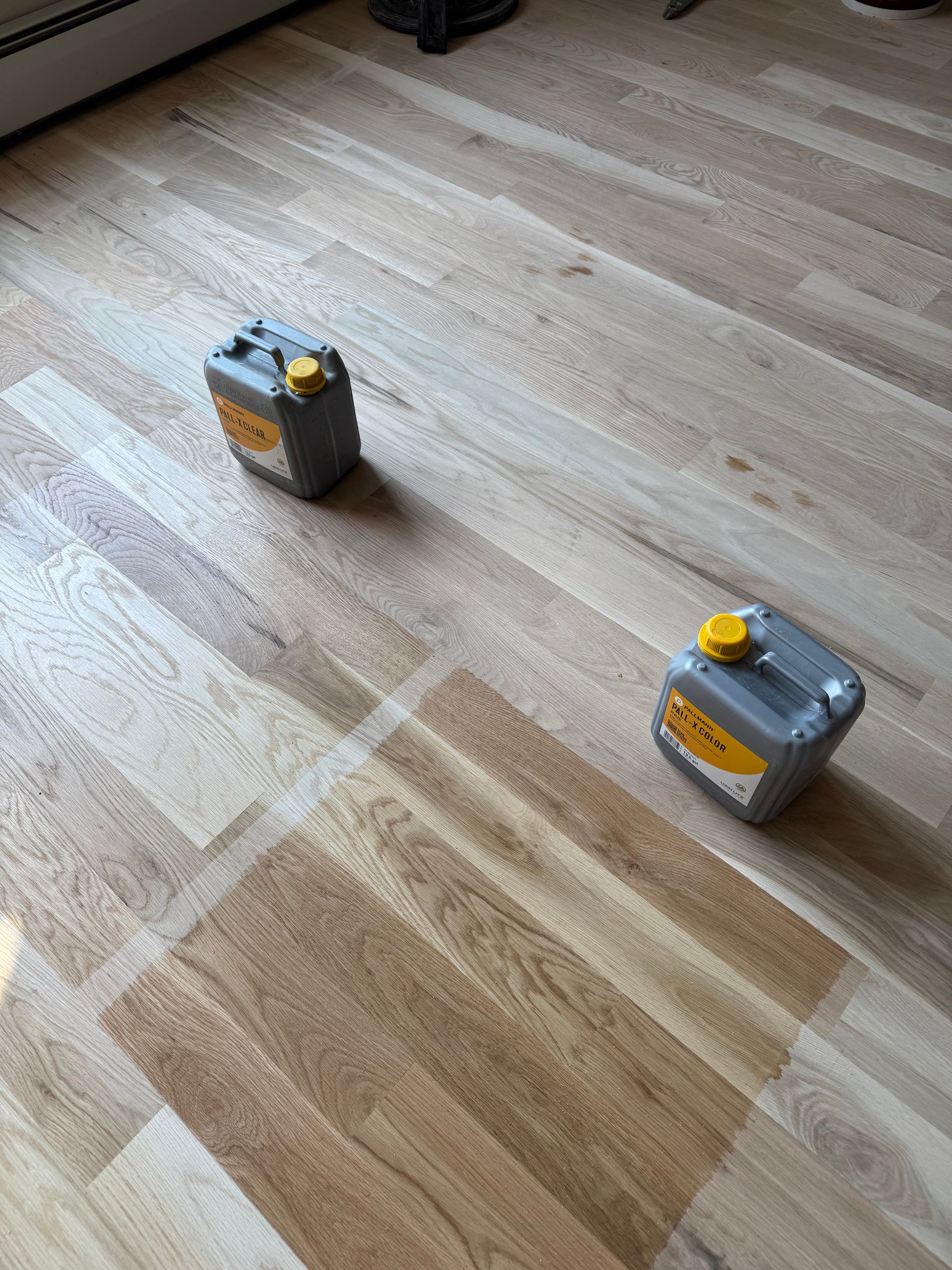 Two small gray containers with yellow caps on a light wood floor, viewed from above.