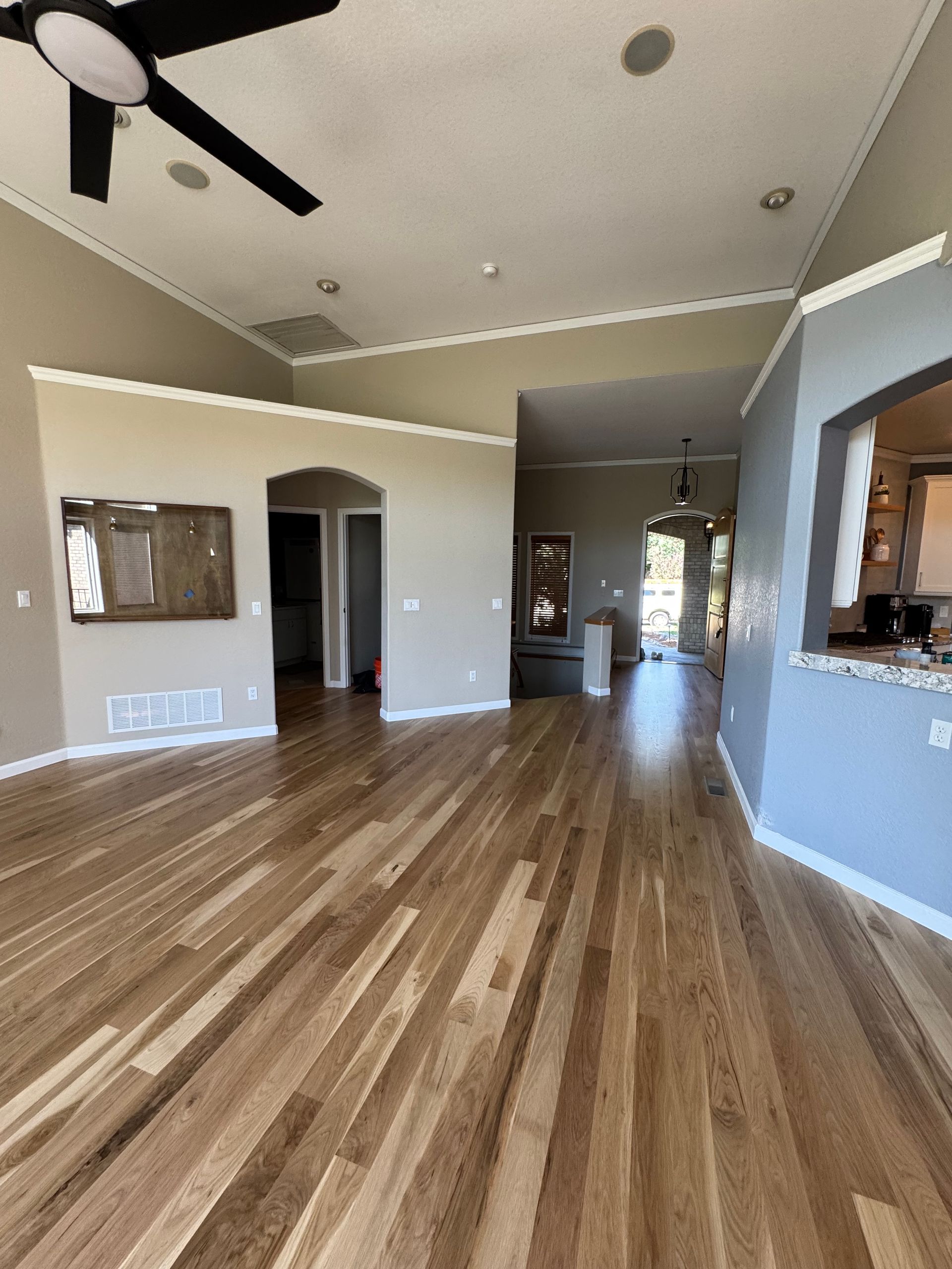 Spacious empty living room with wood floors, vaulted ceiling, ceiling fan, and open archways