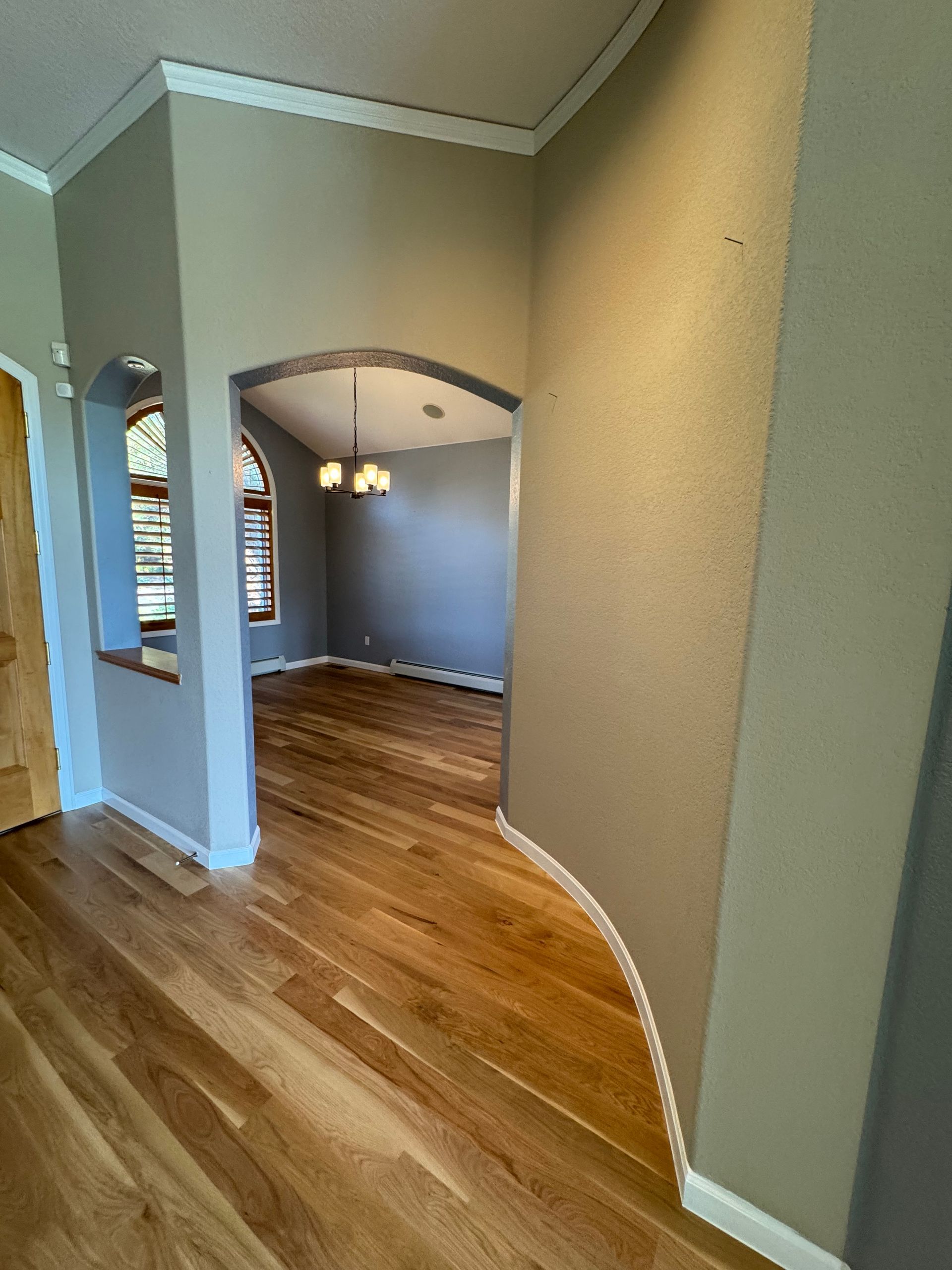 Empty hallway with hardwood floors, beige walls, archways, and a hanging light fixture