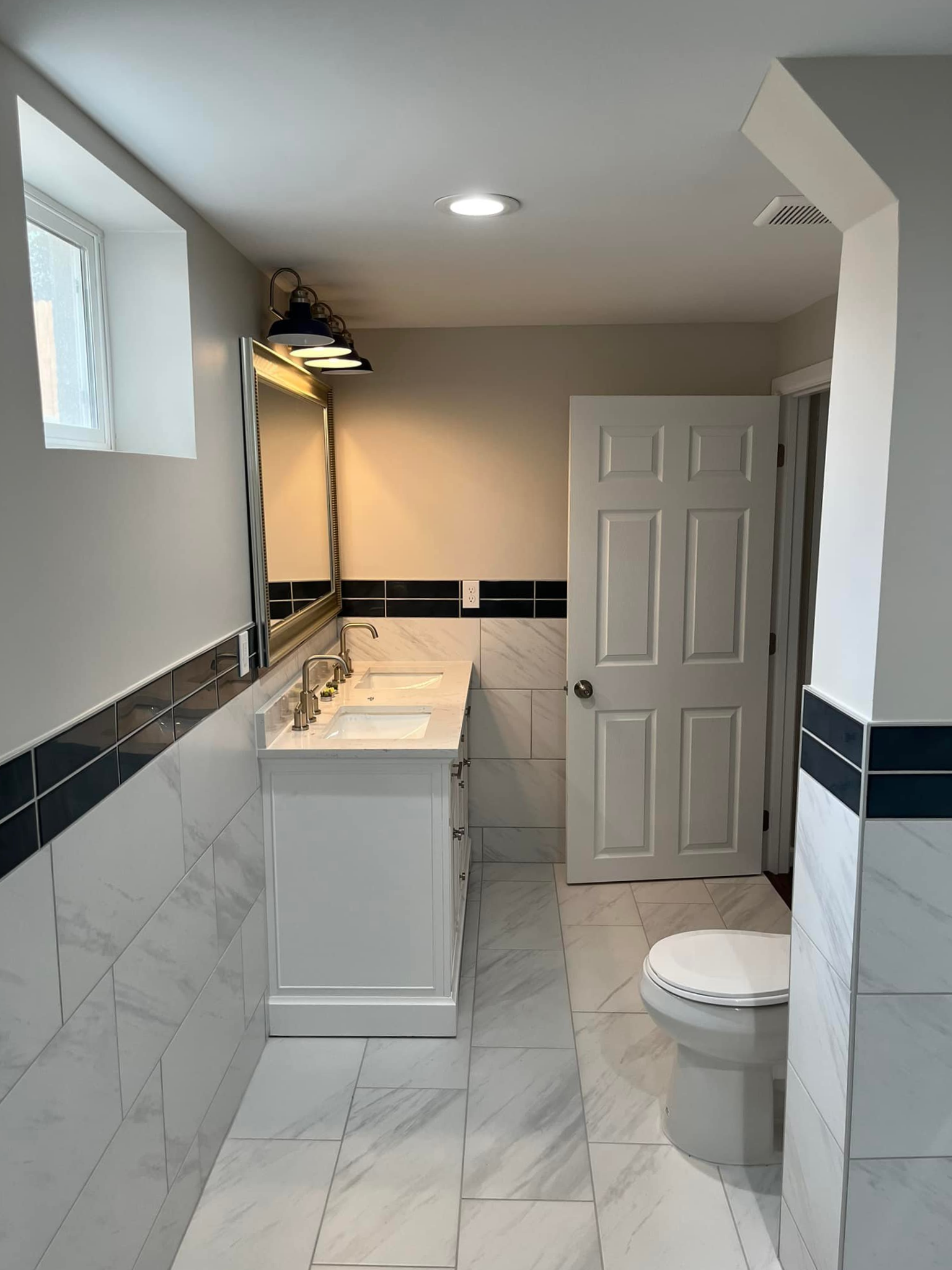 Bright bathroom with marble tile, vanity sink, toilet, and a shower curtain.