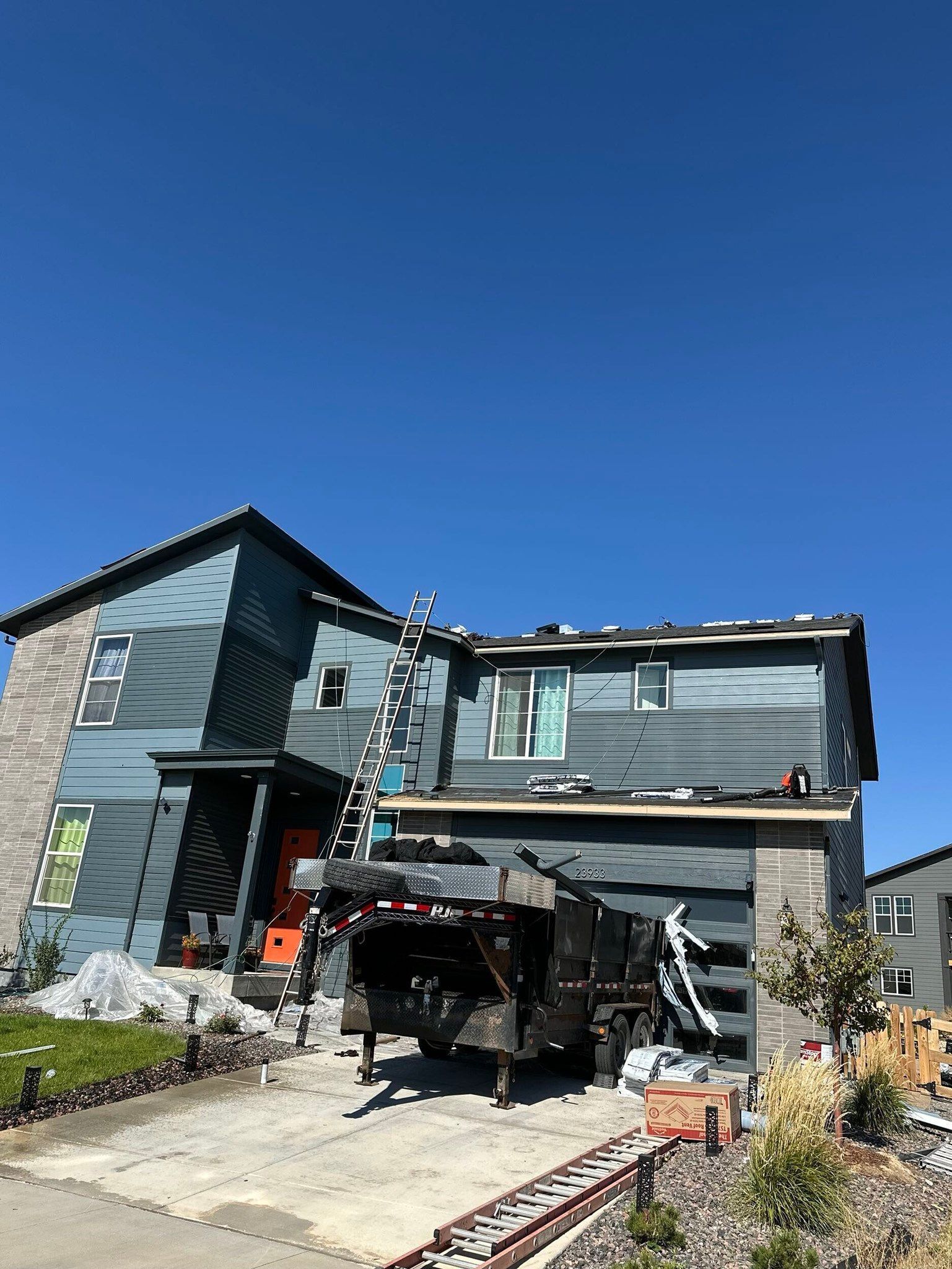Modern two-story house under construction with exposed framing, driveway, and clear blue sky