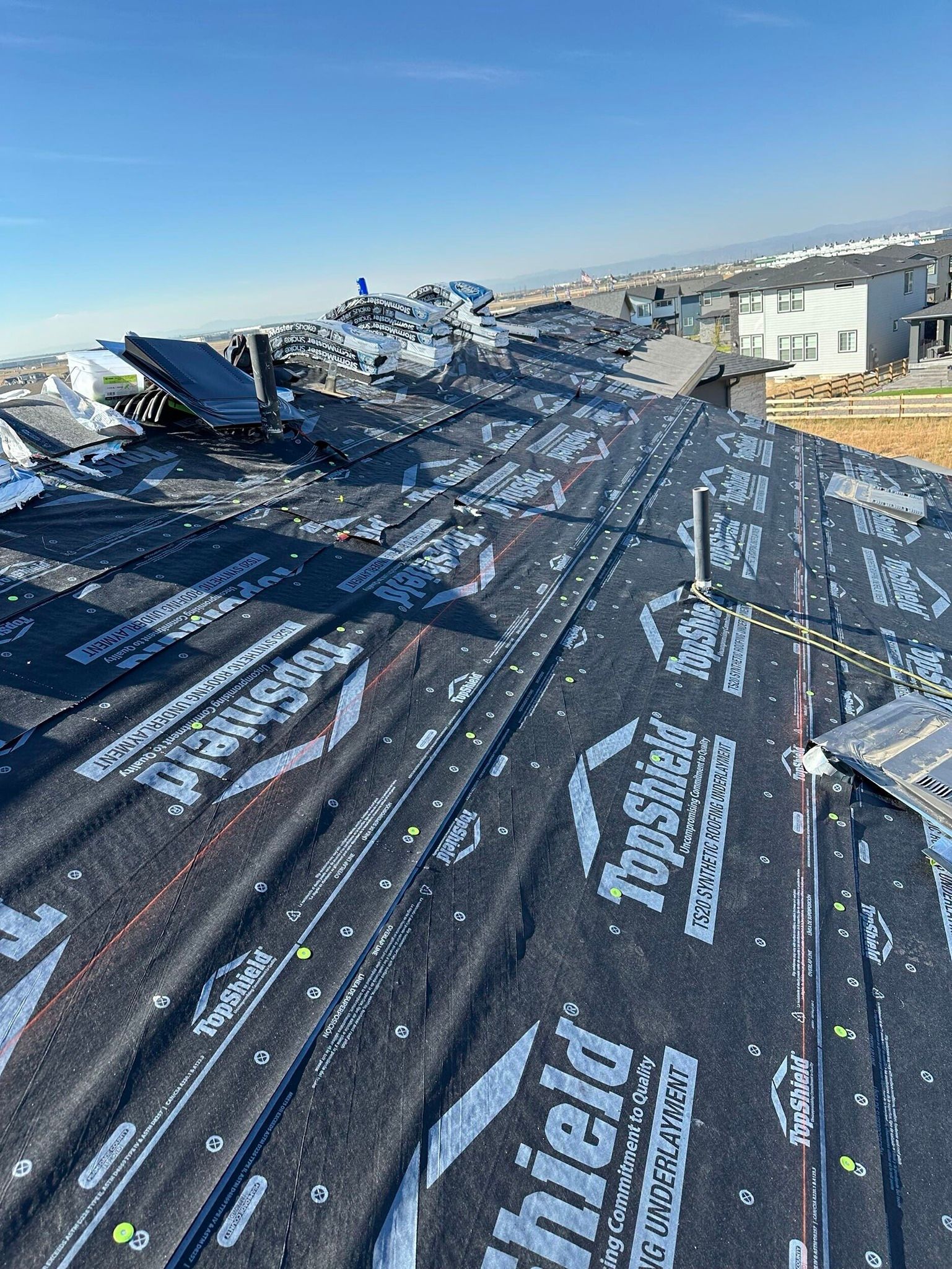 Rooftop underlayment on a sloped roof with HVAC units and buildings under a clear sky.