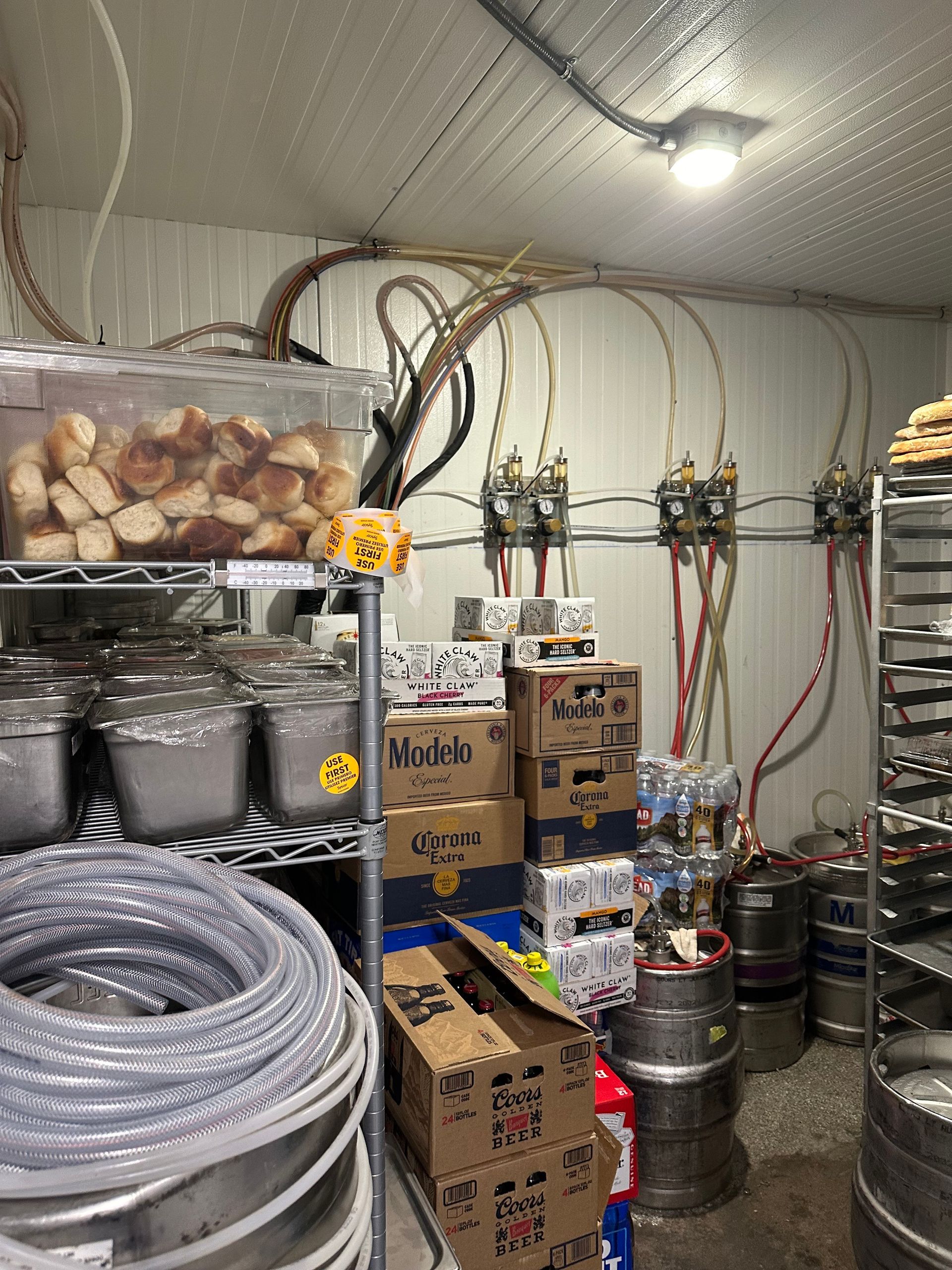 Industrial storage room with stacked metal containers, coiled hoses, boxes, and pipes along the walls