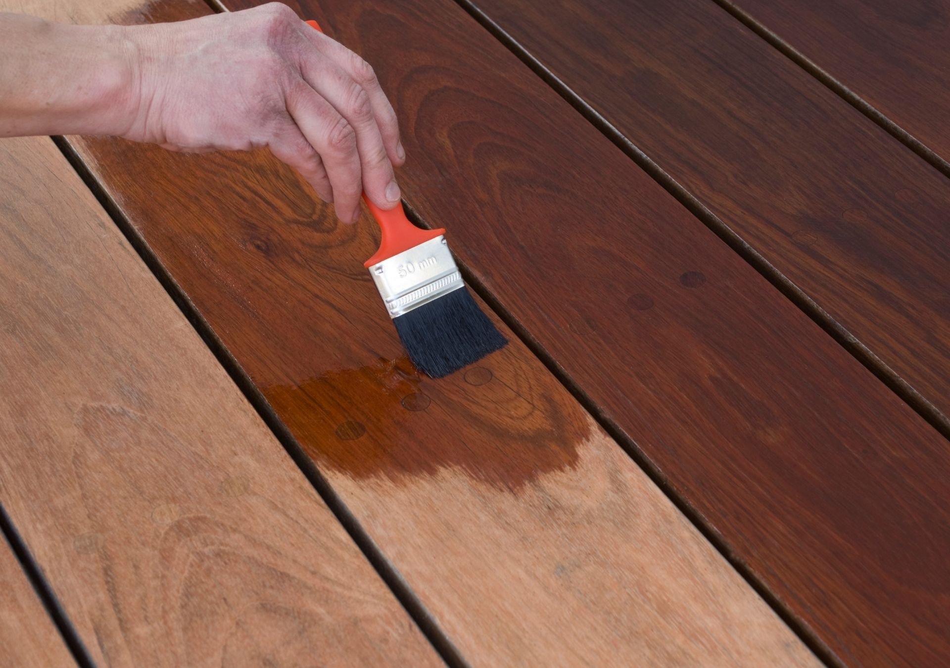 Hand applying stain to a wooden deck board with a paintbrush