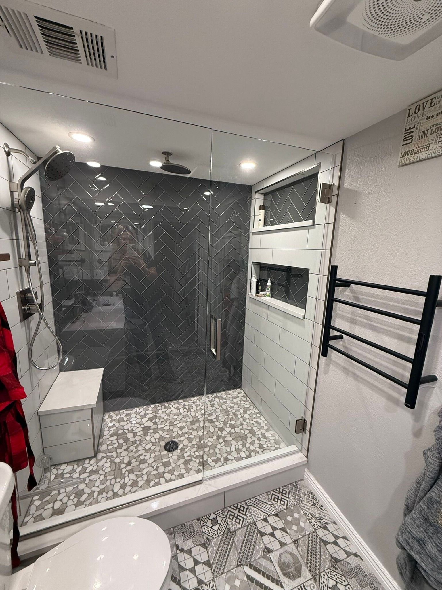 Modern bathroom with walk-in shower, black tile accent wall, white vanity, and patterned floor tiles.