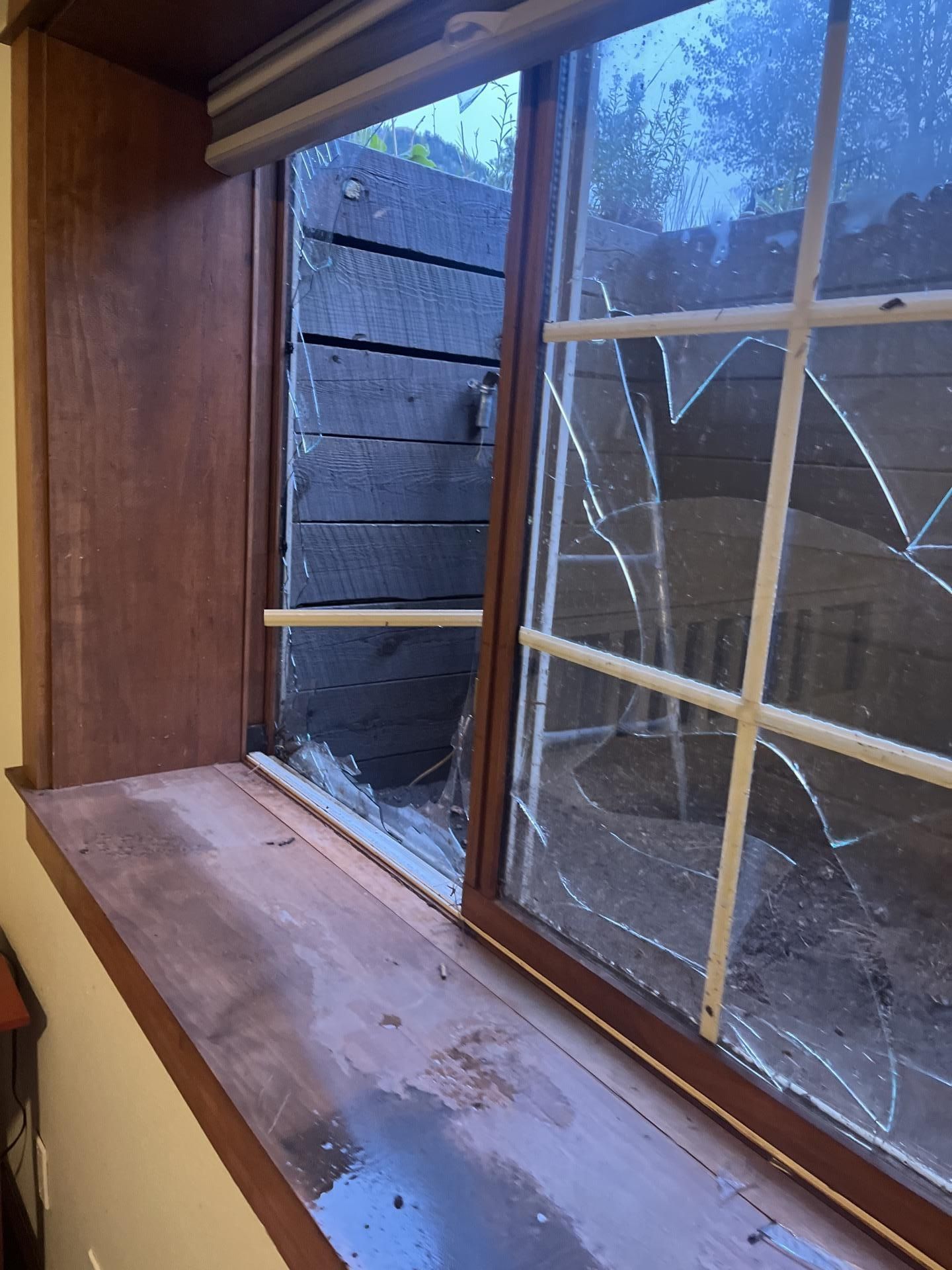 Broken window with cracked panes and wet wooden sill inside a room