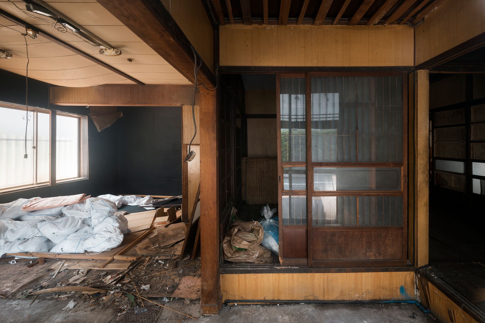 Abandoned, damaged traditional room with tatami mats, exposed beams, and scattered debris