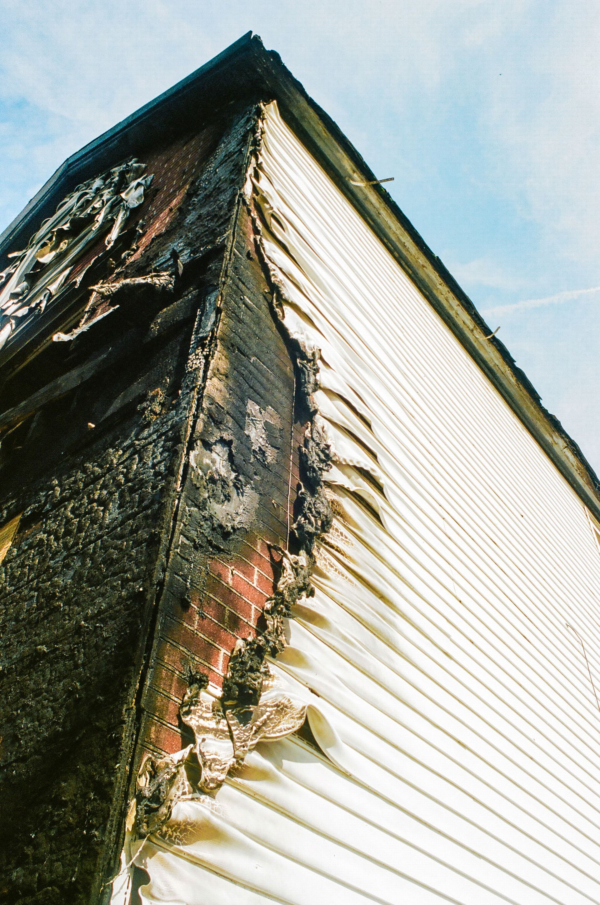 Charred corner of a white house with soot damage against a blue sky