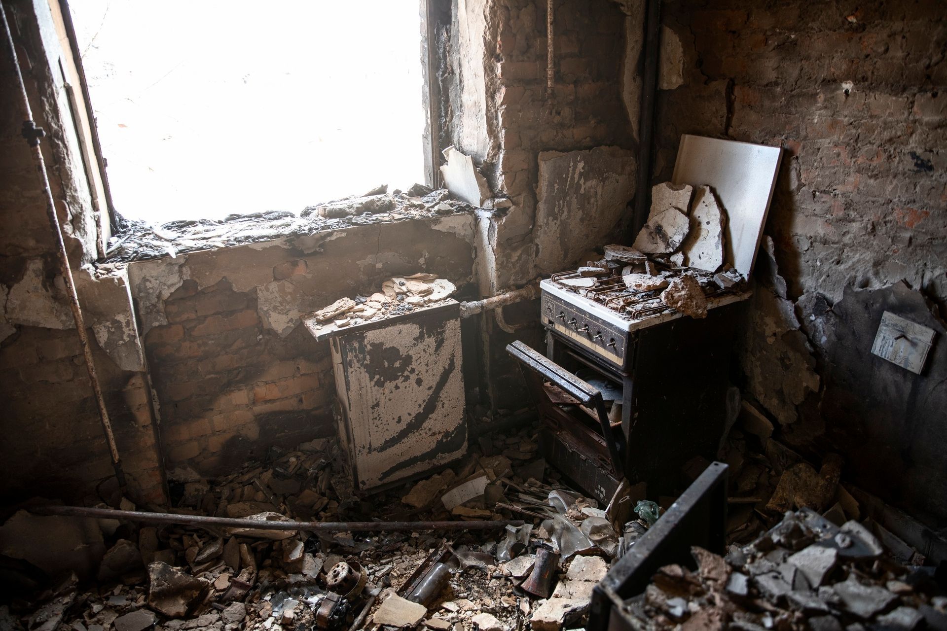 Damaged room with debris, broken window, and toppled furniture in a dim, abandoned interior
