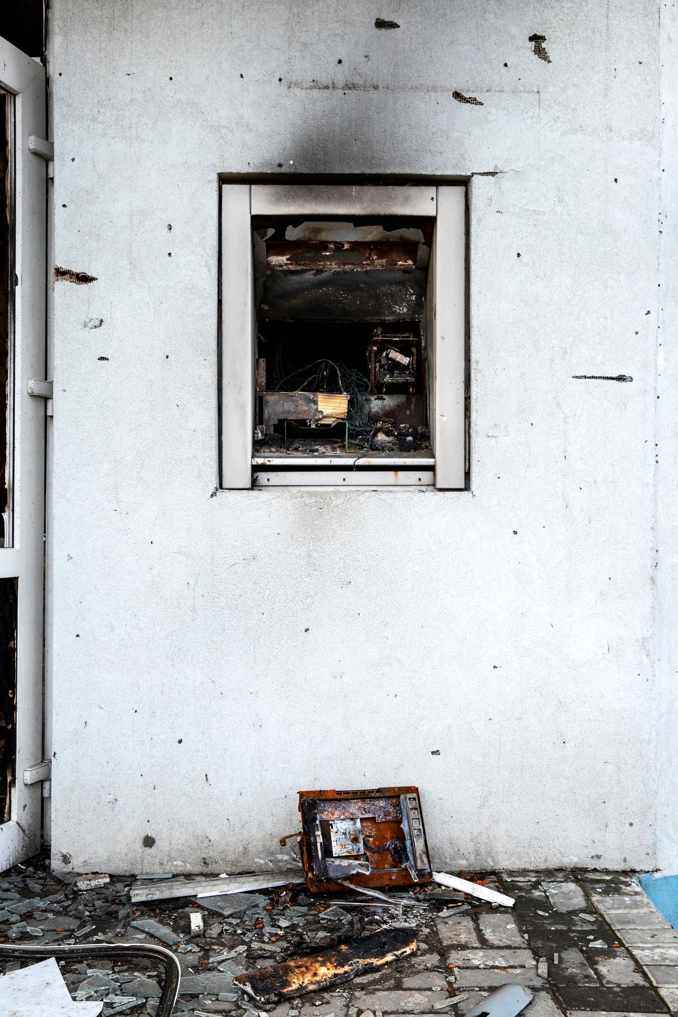 Charred fireplace opening in a damaged white wall with ash and debris on the floor