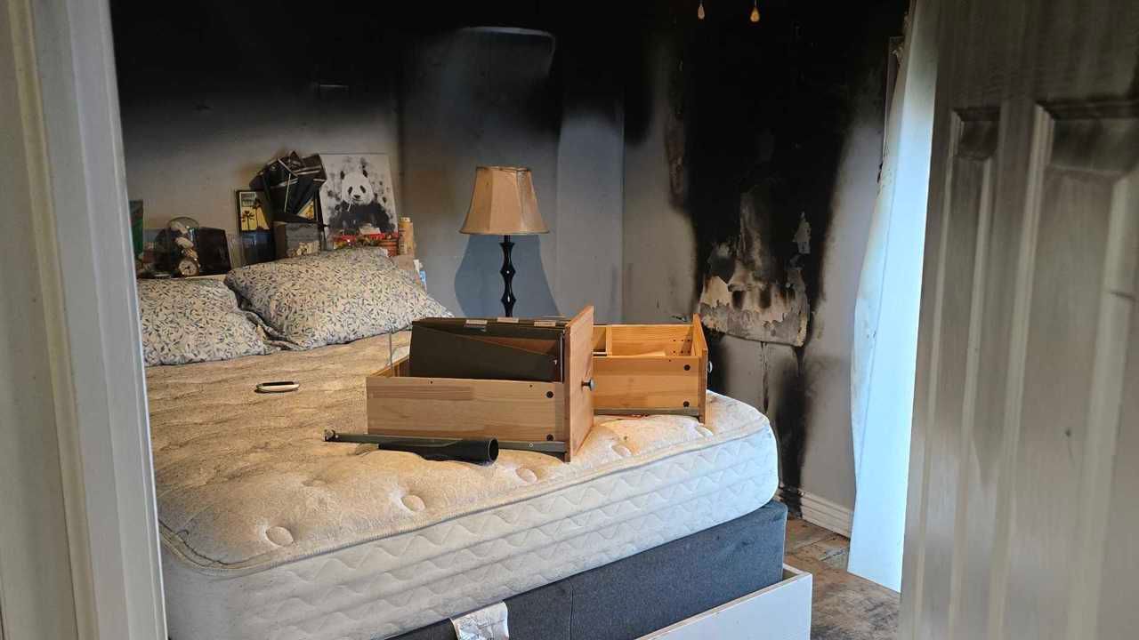Bedroom with an unmade bed, cardboard box on the mattress, lamp on a nightstand, and open closet doors.