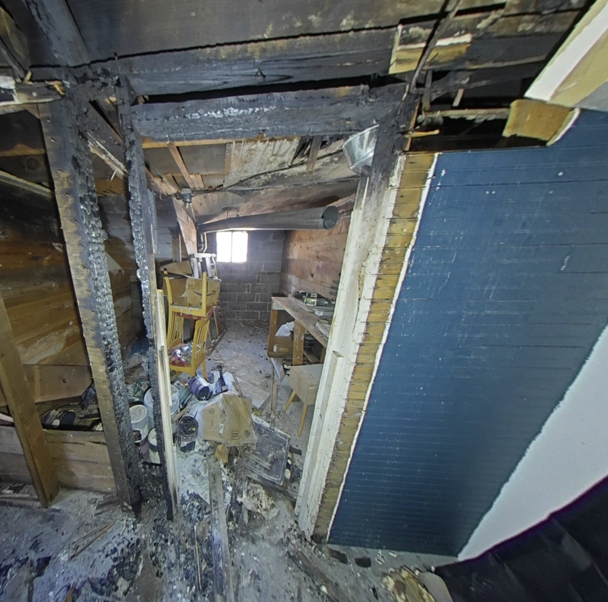 Damaged interior room with collapsed ceiling, exposed beams, debris, and a small window in the back.