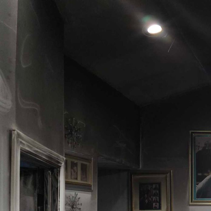 Dim hallway ceiling with a recessed light above framed wall decor and cabinets.