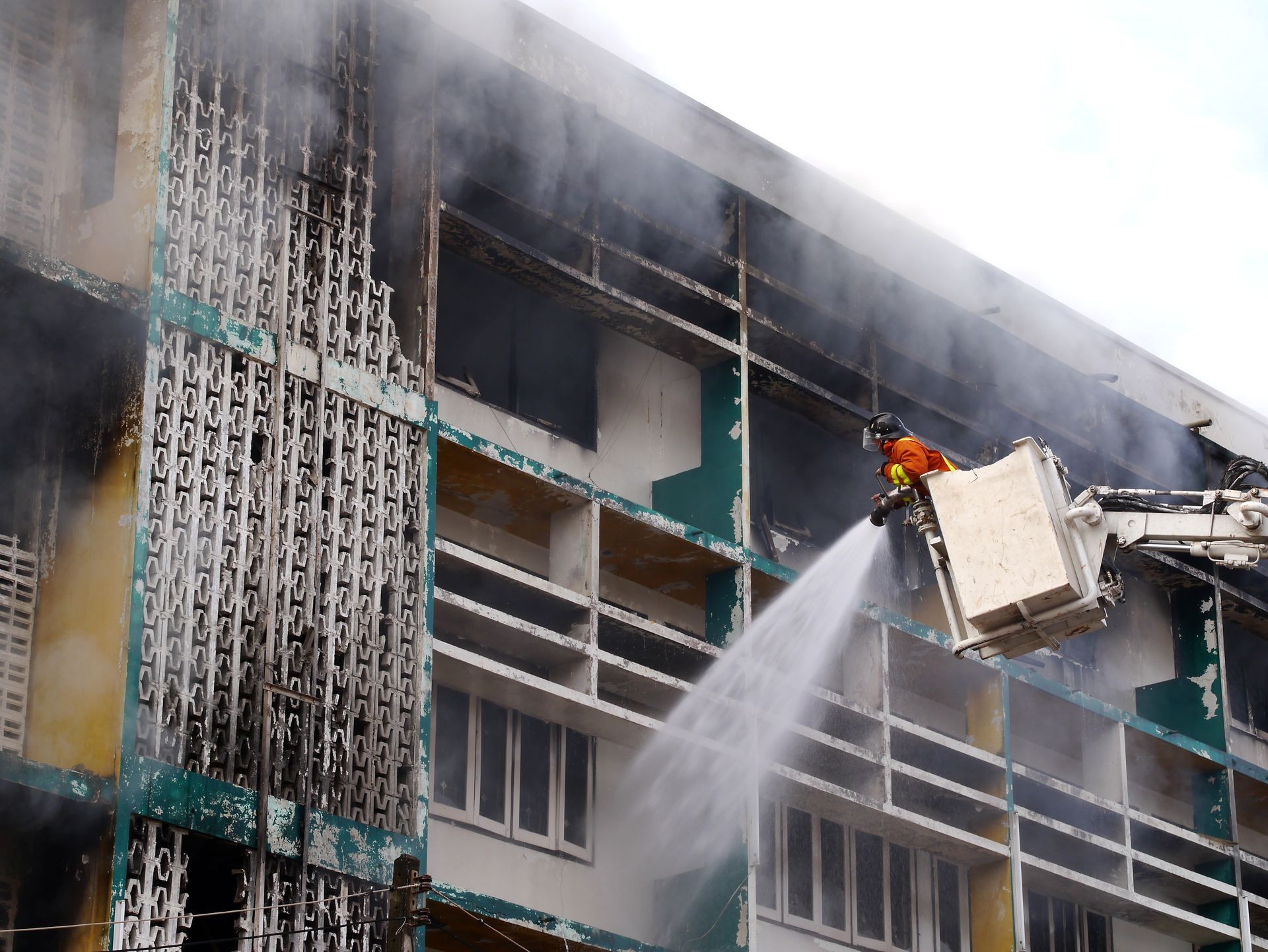 Firefighter spraying water from a lift basket on a smoke-filled building facade