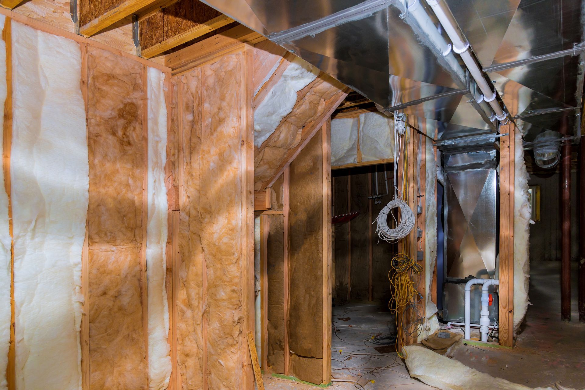 Dim basement with wood framing, plastic sheeting, exposed pipes, and a hanging light fixture