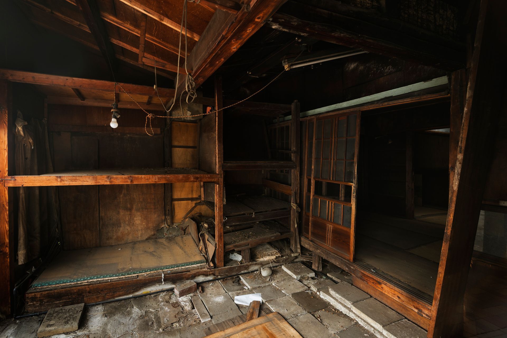 Dilapidated wooden interior with broken floorboards, debris, and dark empty rooms