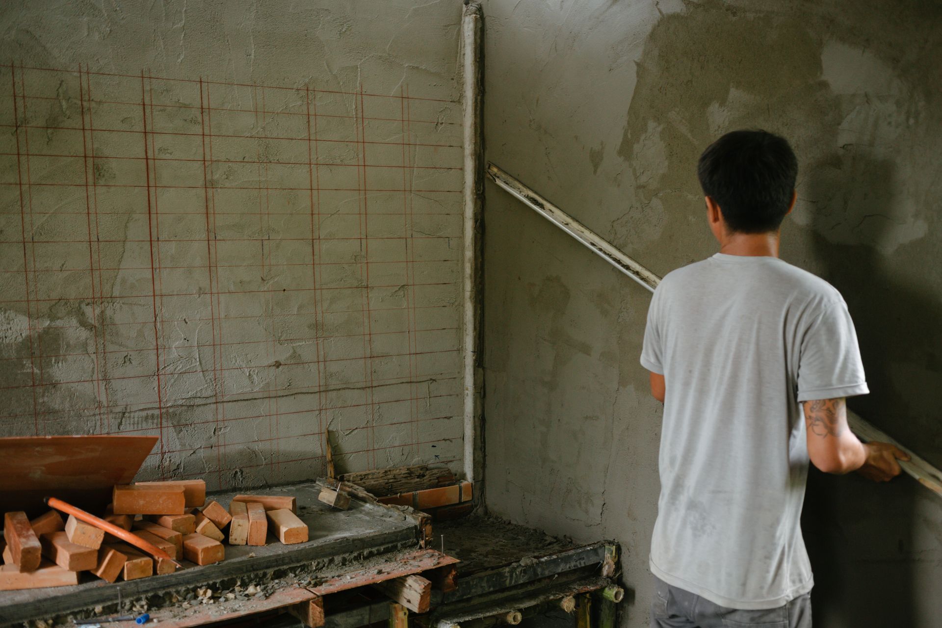 Person standing in an unfinished room beside a wall being plastered, with bricks and tools on a workbench.