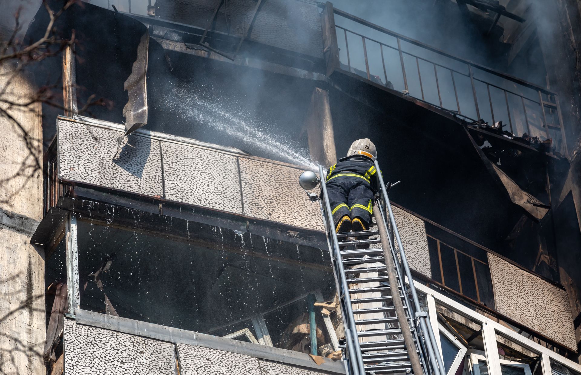 Firefighter climbing ladder toward smoke-filled, burning building balcony
