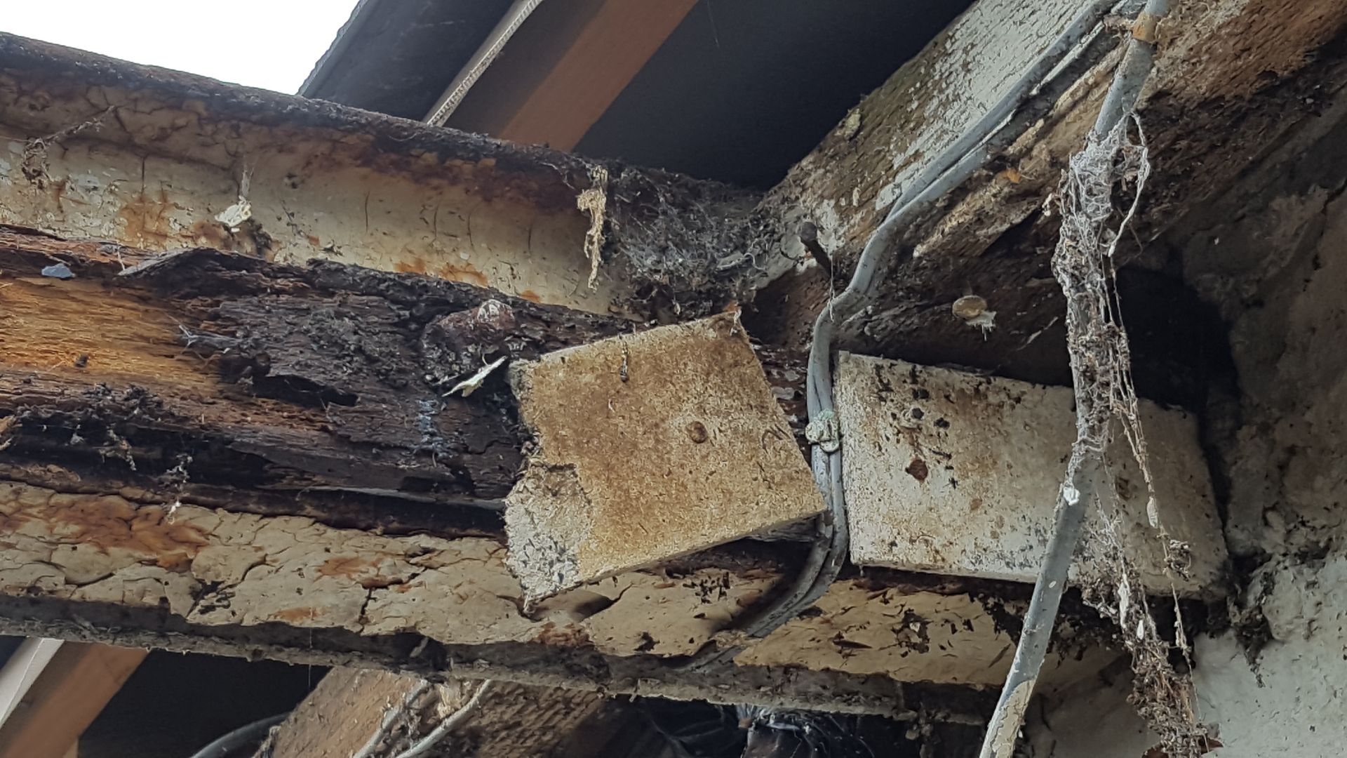 Charred, water-damaged wooden roof beams with debris and damaged insulation.