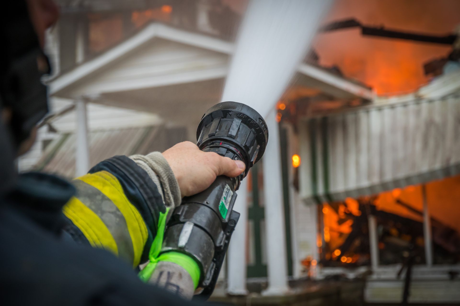 Firefighter spraying water at a house engulfed in flames and smoke