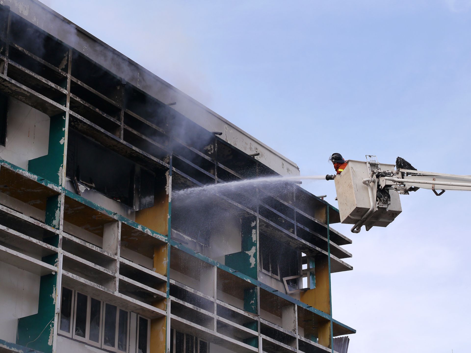 Firefighters spray water from a ladder truck onto a smoky building exterior.