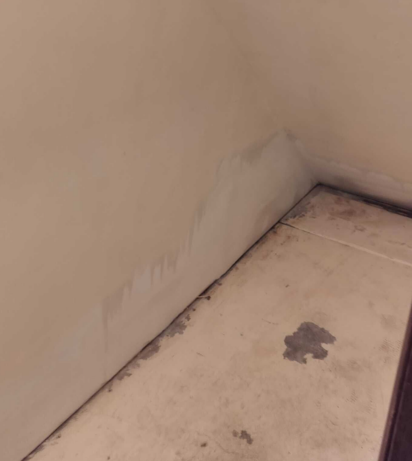 Damaged wall corner with peeling paint and water stains on a stained floor