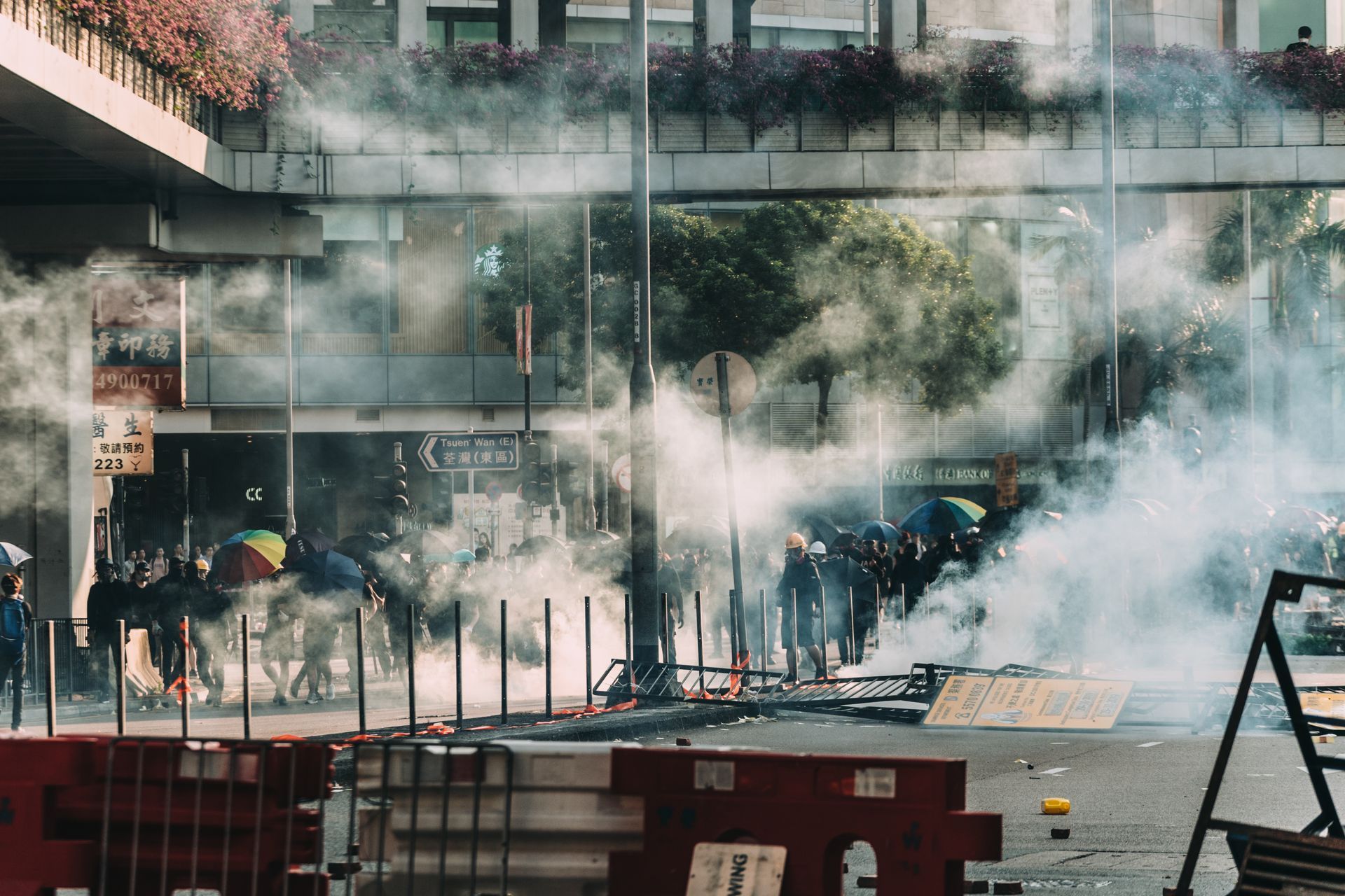 People on a smoky street behind barricades, with debris and a building in the background