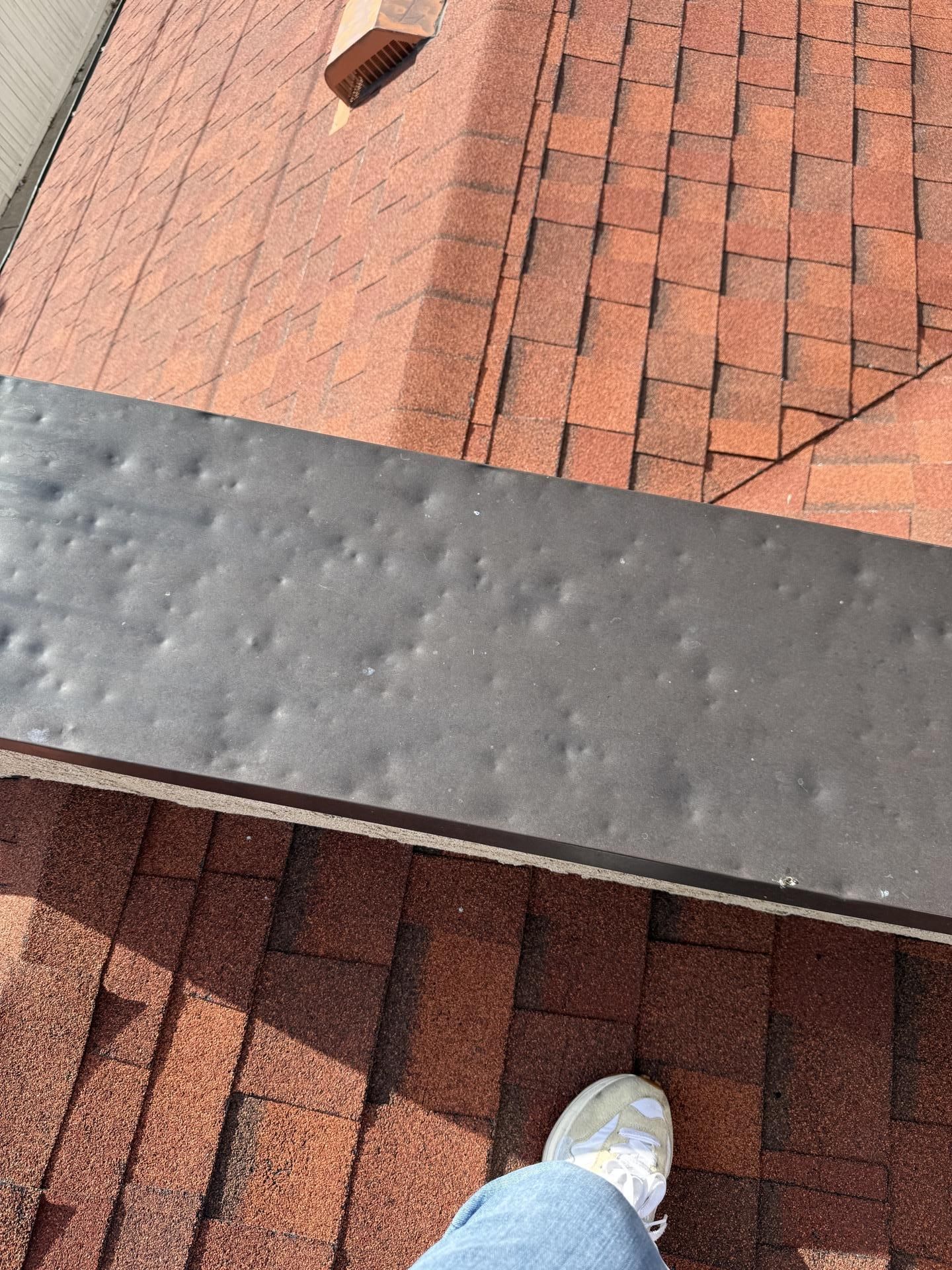 Roof shingles with a black ridge vent and part of a person’s shoe at the bottom edge