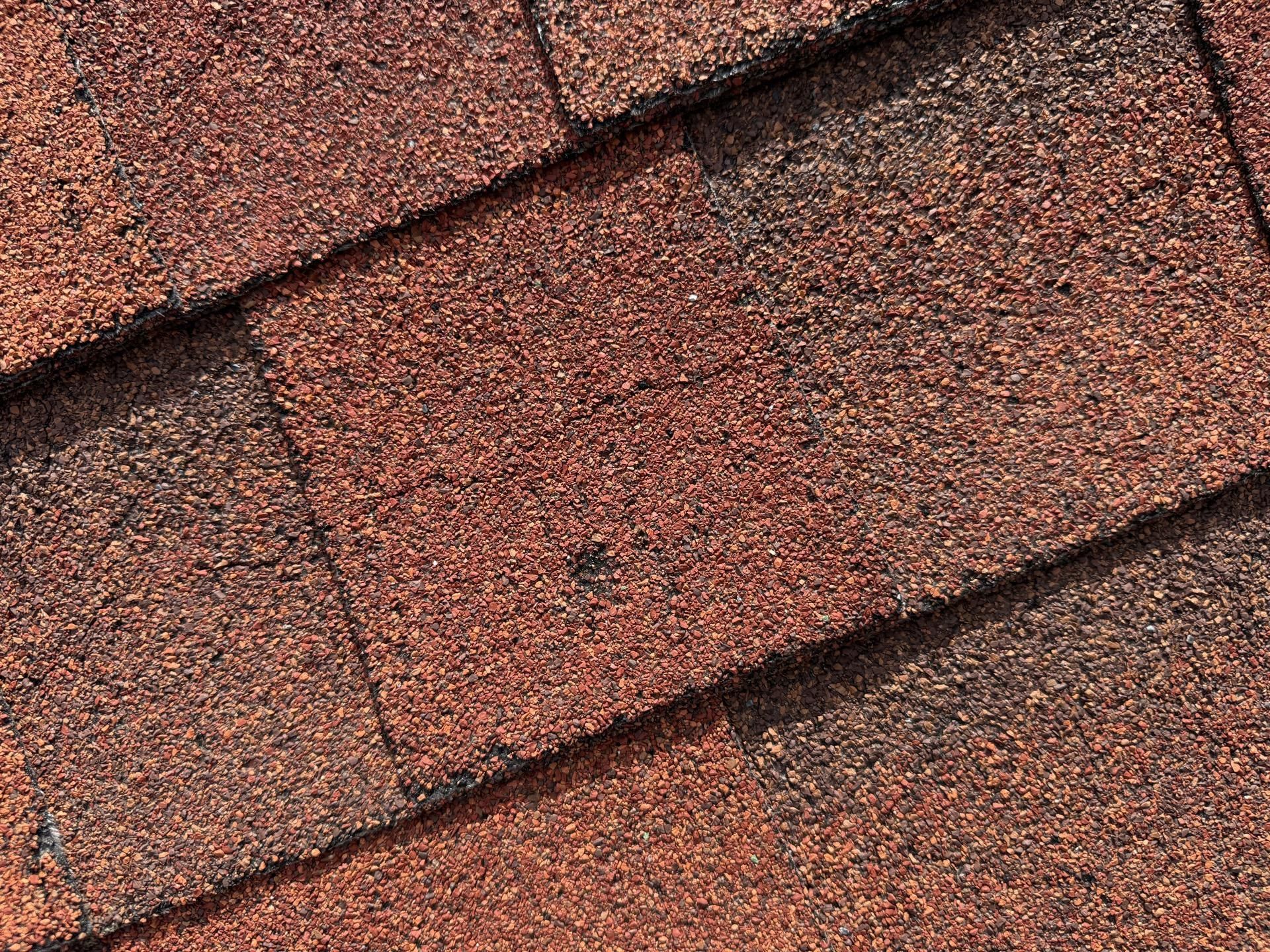 Close-up of reddish-brown roof shingles with a small dark hole in the center.
