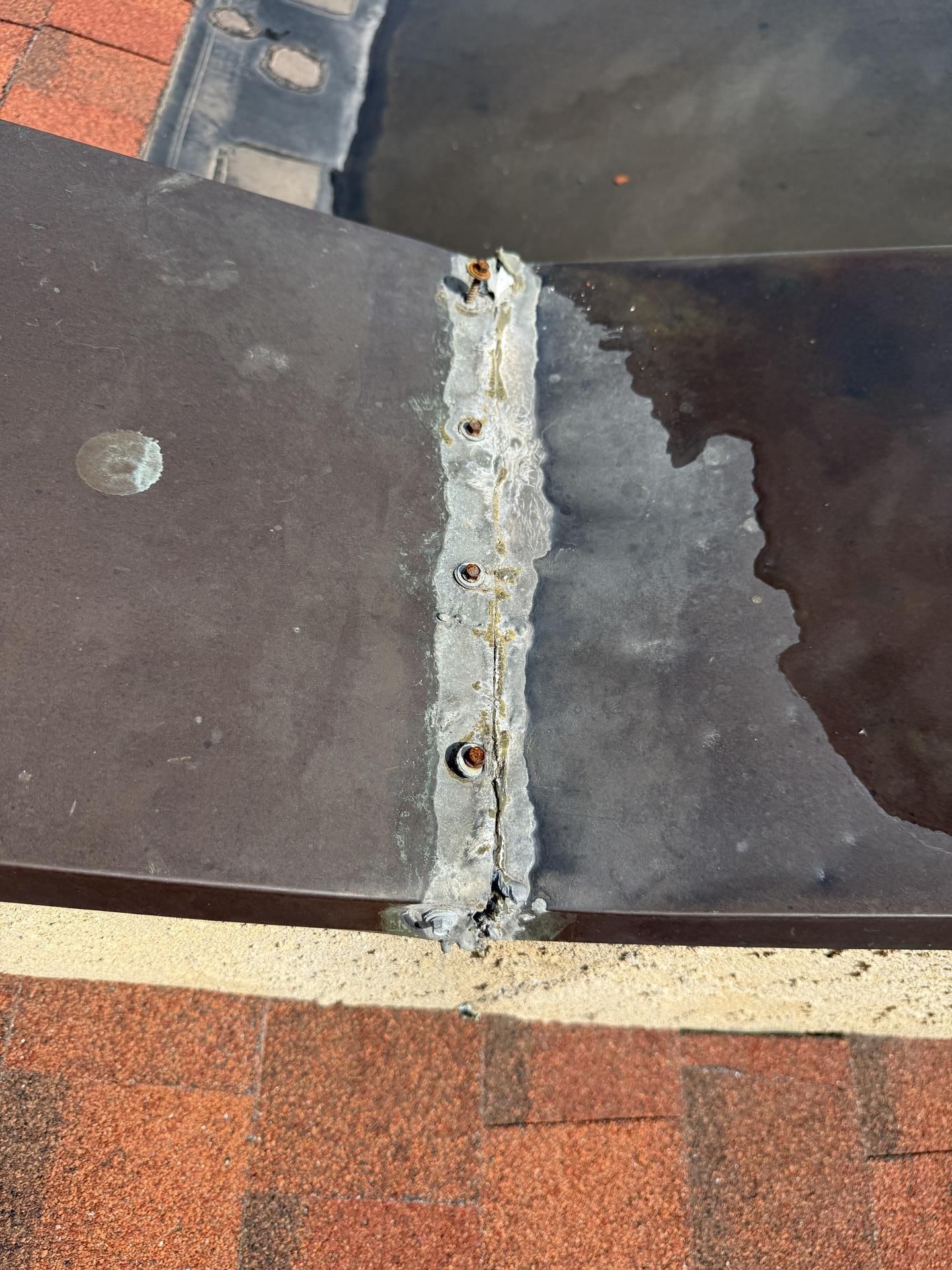 Close-up of a roof seam with cracked gray sealant between dark shingles and red tiles.